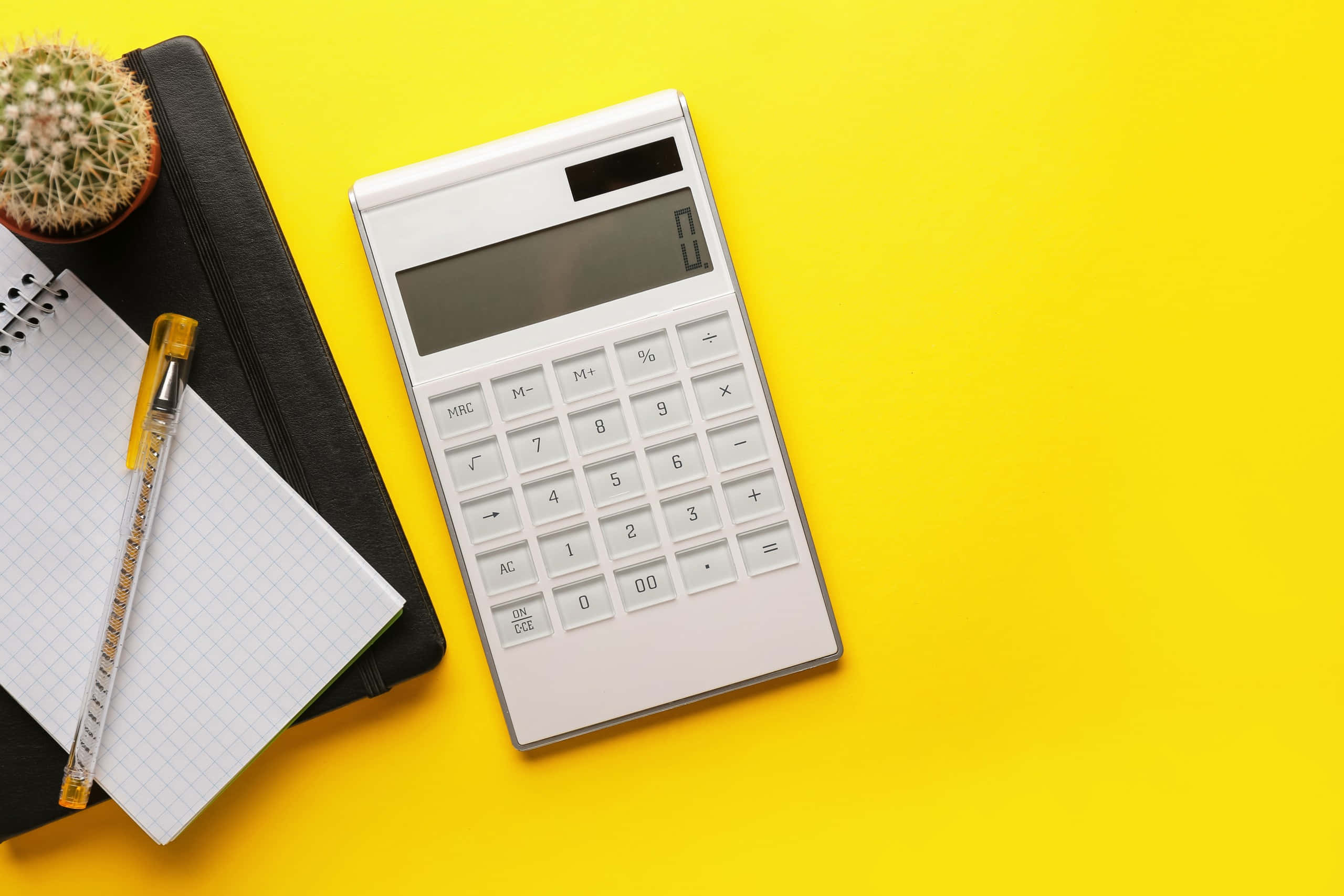 Calculator 桌布 壁紙 — 一個白色計算器放在一本筆記本、一支筆和一個小仙人掌旁邊，置於亮黃色表面上。