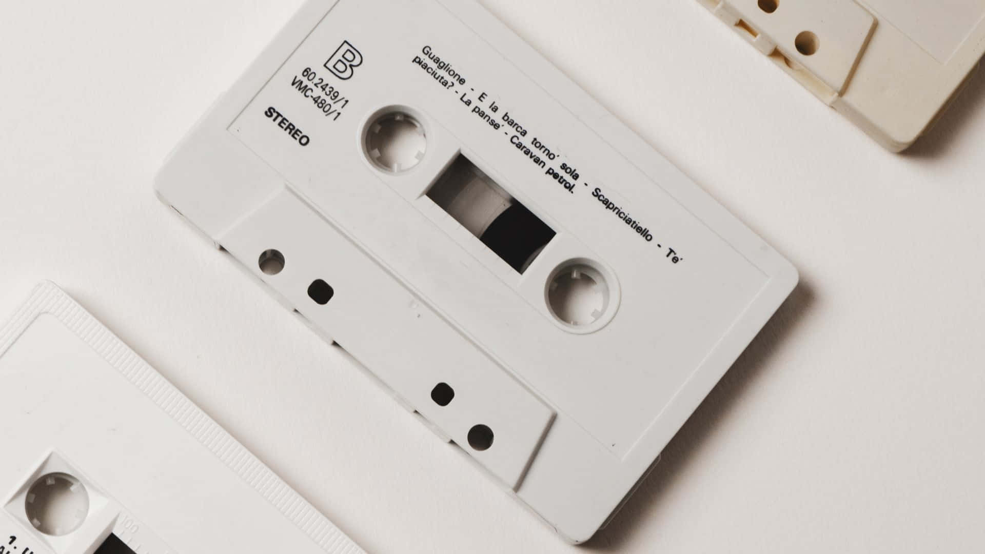 音樂美學 桌布 壁紙 — 一個白色錄音帶，帶有可見的曲目標籤，放在純白色表面上，喚起對模擬音樂的懷舊感。