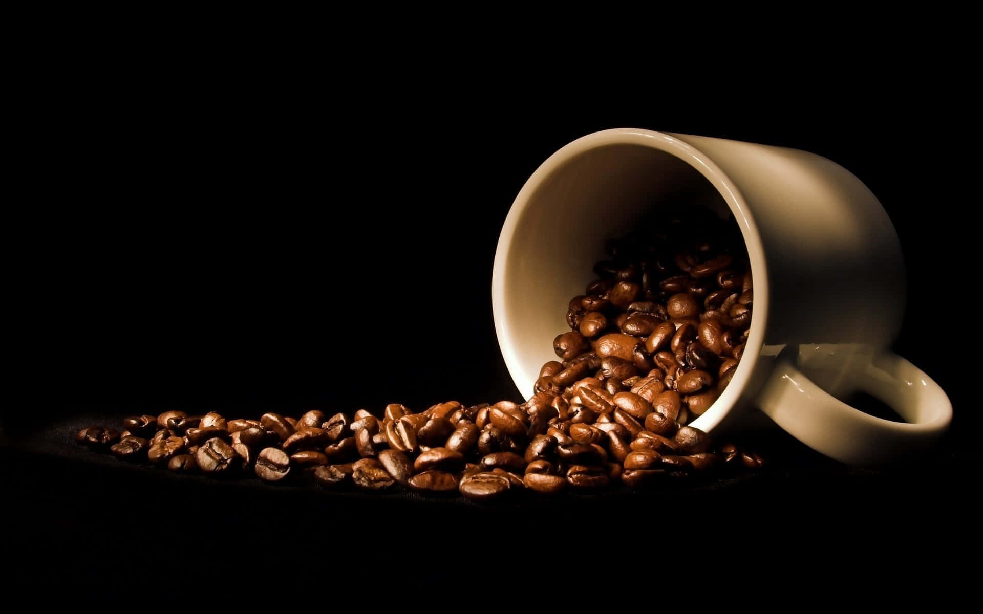 Black Coffee 桌布 壁紙 — 一個白色陶瓷杯在戲劇性的攝影棚燈光下，將濃郁的棕色咖啡豆灑落在純黑色背景上。