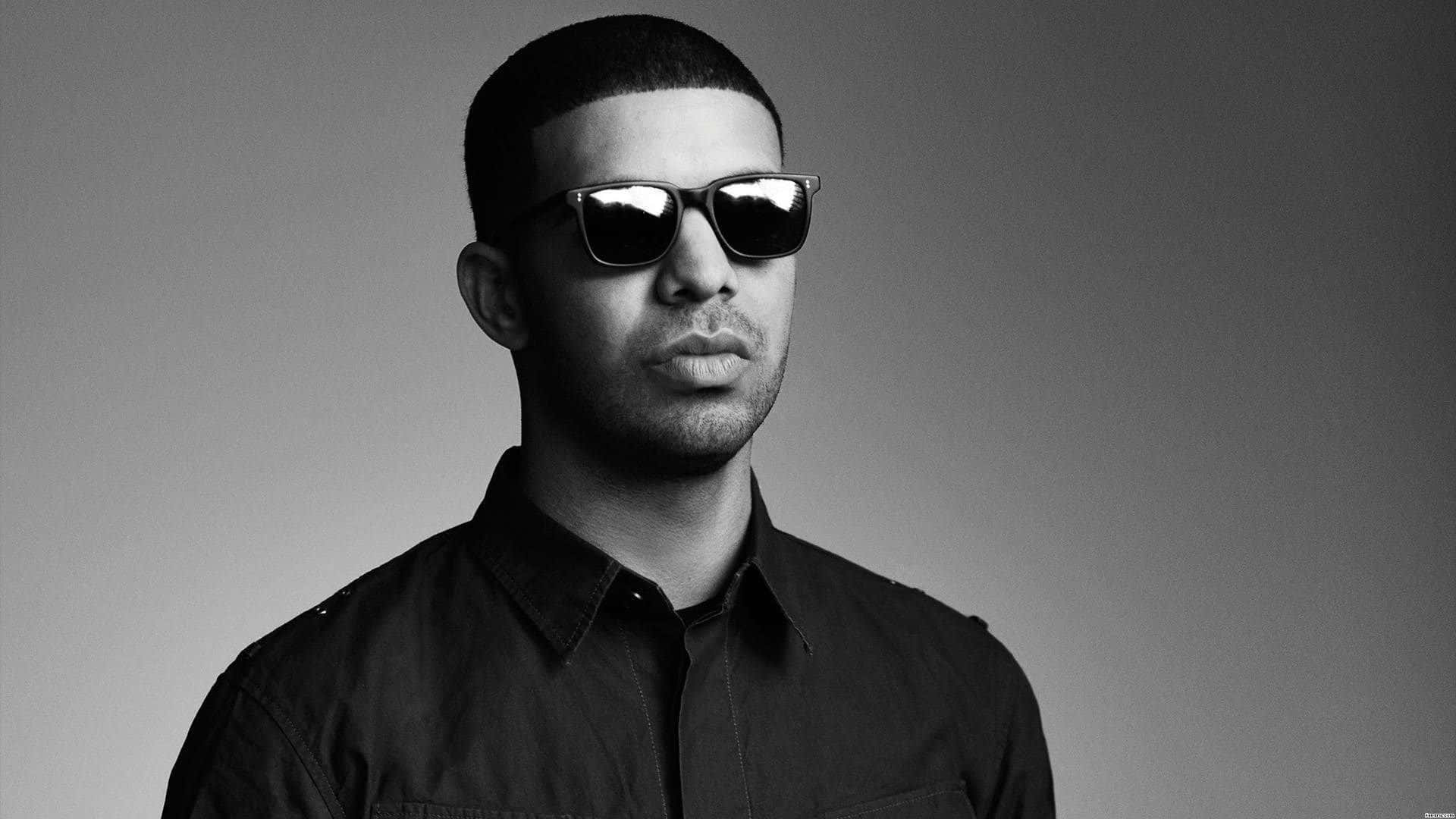 Drake 桌布 壁紙 — 一個短髮男子戴著深色太陽眼鏡，在純灰色背景前的黑白肖像。