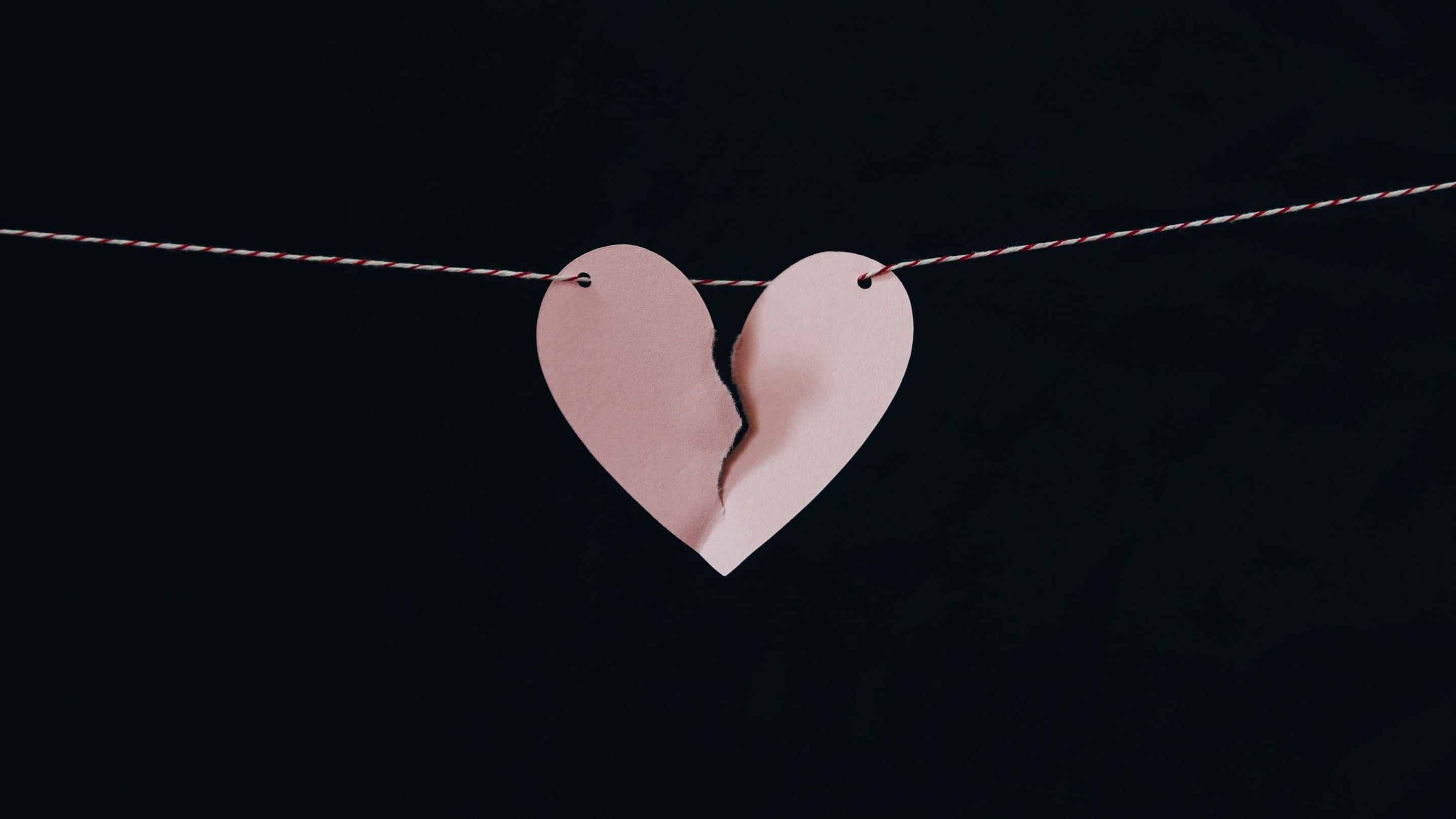 Broken Heart Black 桌布 壁紙 — 一個破爛的粉紅色紙心心掛在一條紅白相間的繩子上，背景是純黑色。