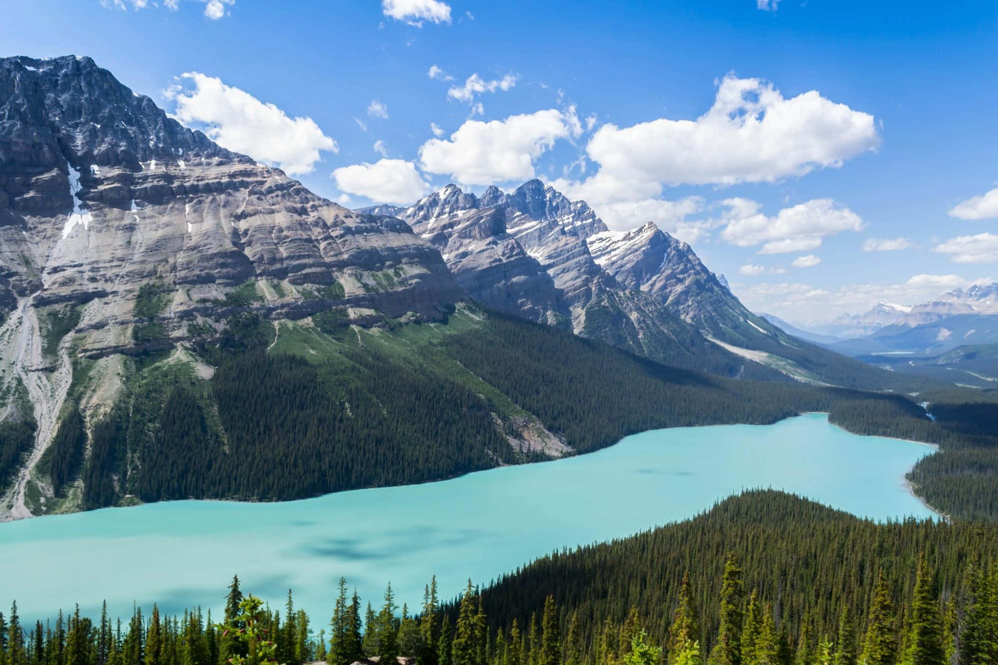 Canada 桌布 壁紙 — 一個碧綠色的湖泊坐落在高聳的雪山之間，上方是明亮的藍天和蓬鬆的白雲。