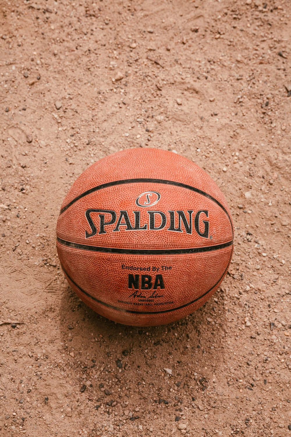 ball 桌布 壁紙 — 一個磨損的橙色 Spalding NBA 籃球在自然光下放在粗糙的紅褐色泥土上。