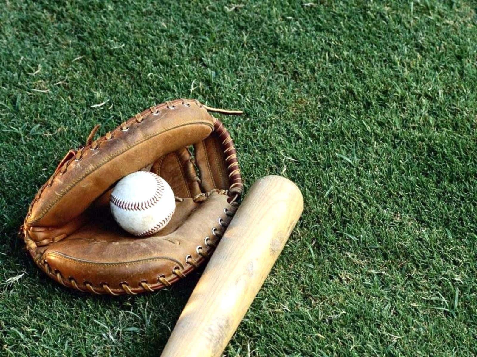 baseball bat 桌布 壁紙 — 一個磨損的皮革棒球手套在鮮綠色的草地上，旁邊放著一個白色棒球和一支木製球棒。