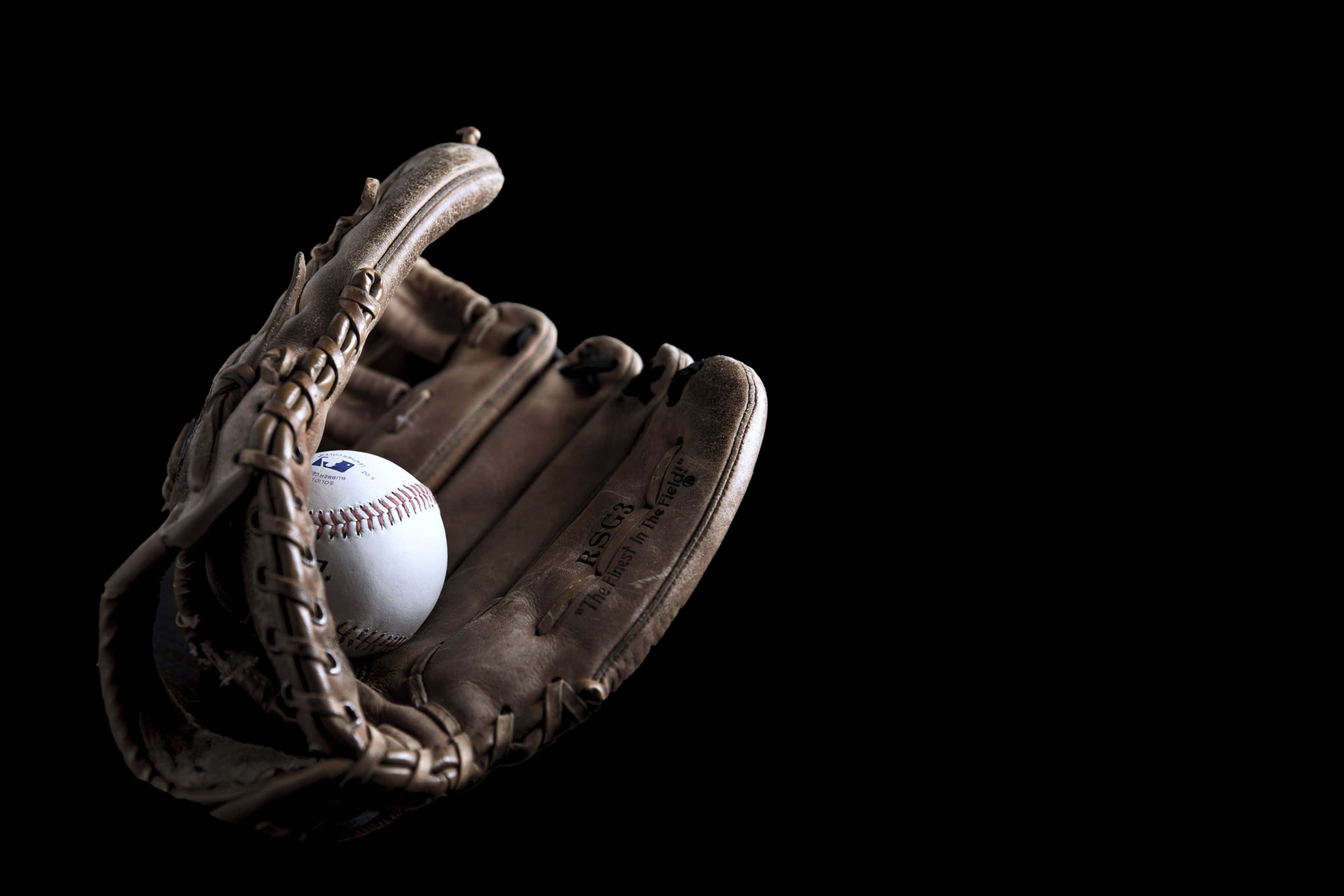 Baseball Gloves 桌布 壁紙 — 一個磨損的皮革棒球手套托著一個白色棒球，背景是純黑色。