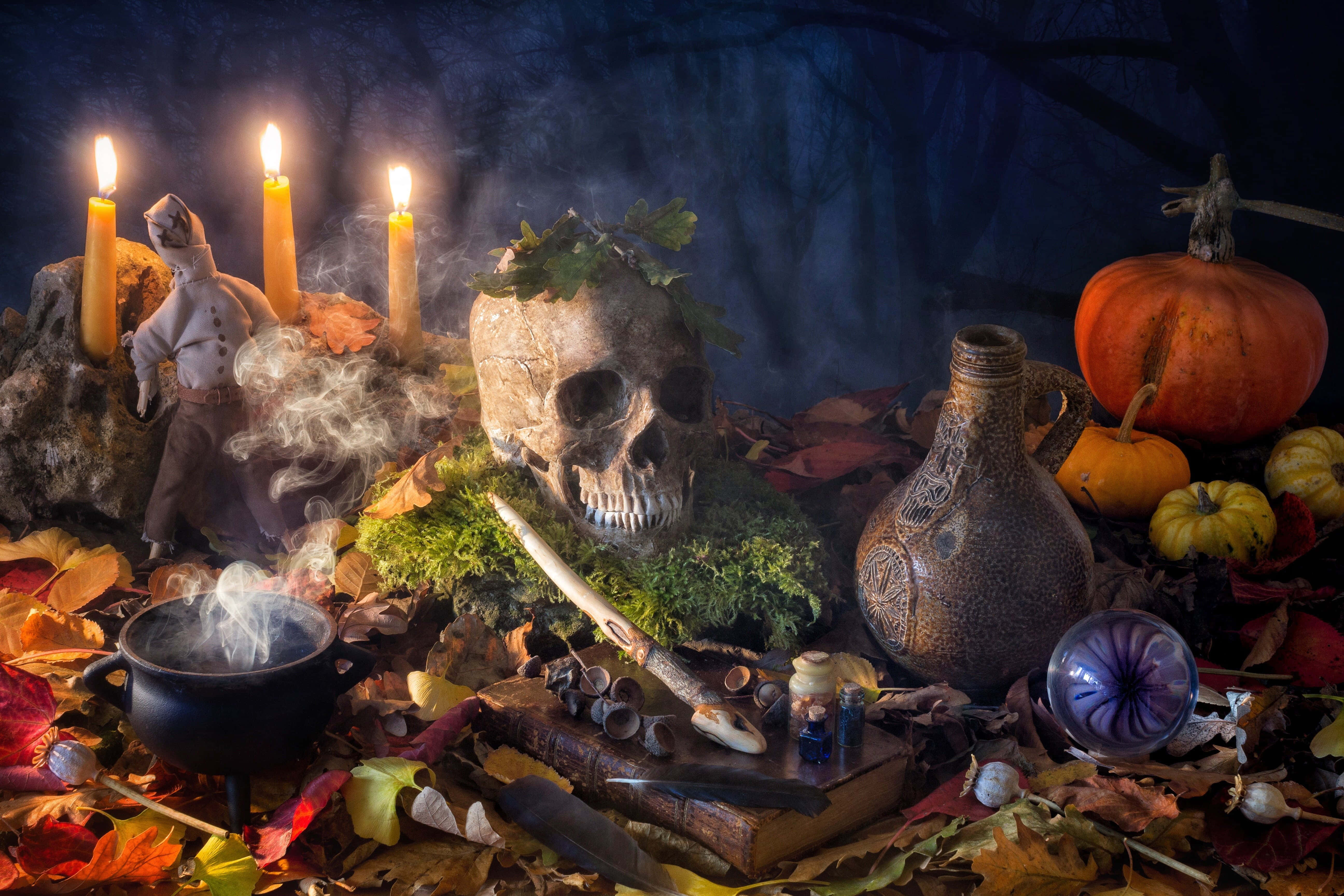 Grimoire 桌布 壁紙 — 一個神秘的秋季祭壇，有頭骨、發光的蠟燭、南瓜和冒煙的大鍋，散落在落葉中。