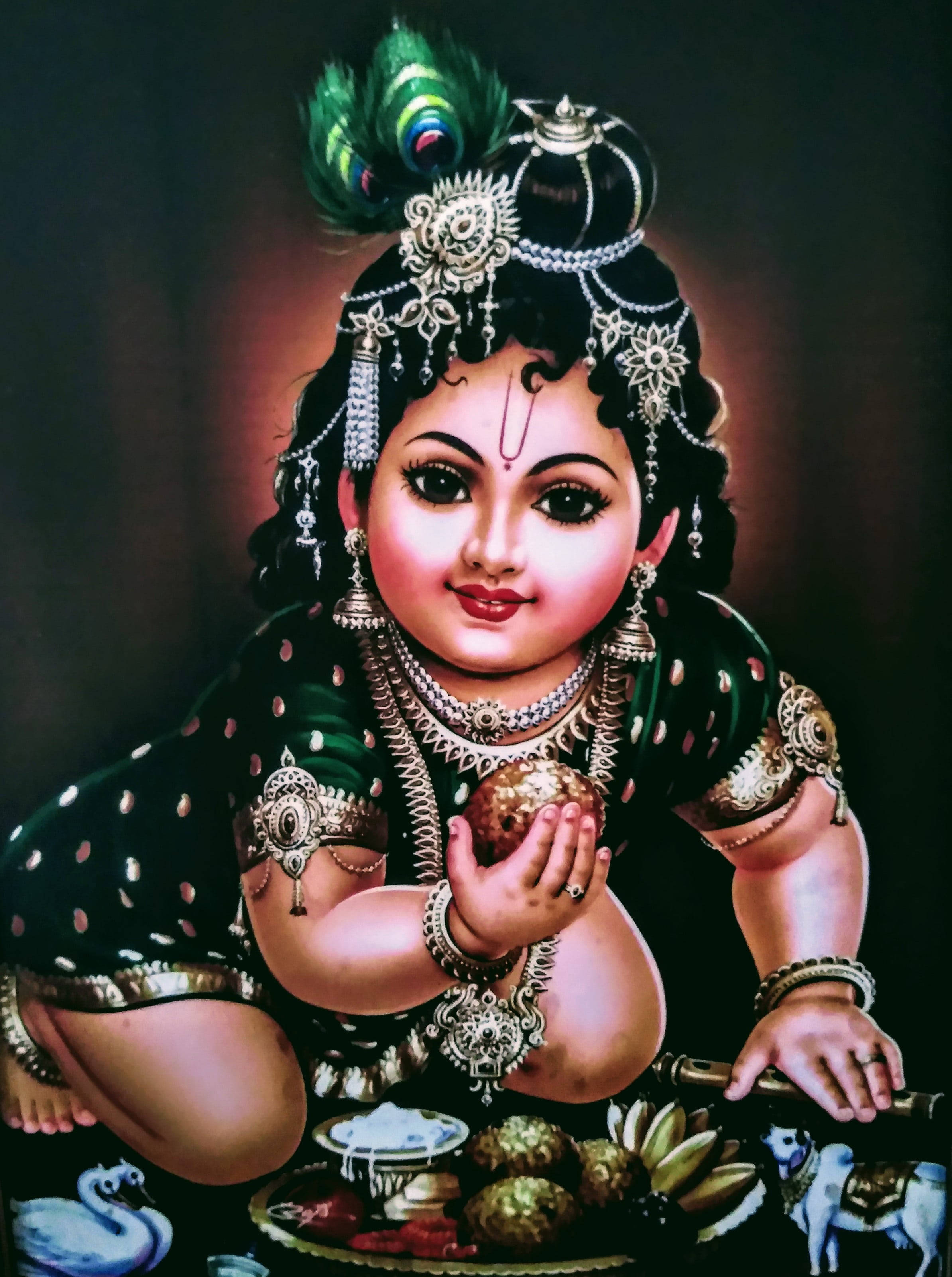 krishna phone 桌布 壁紙 — 一個神聖的孩子，裝飾著精緻的珠寶和孔雀羽毛冠冕，帶著寧靜的微笑拿著甜點。