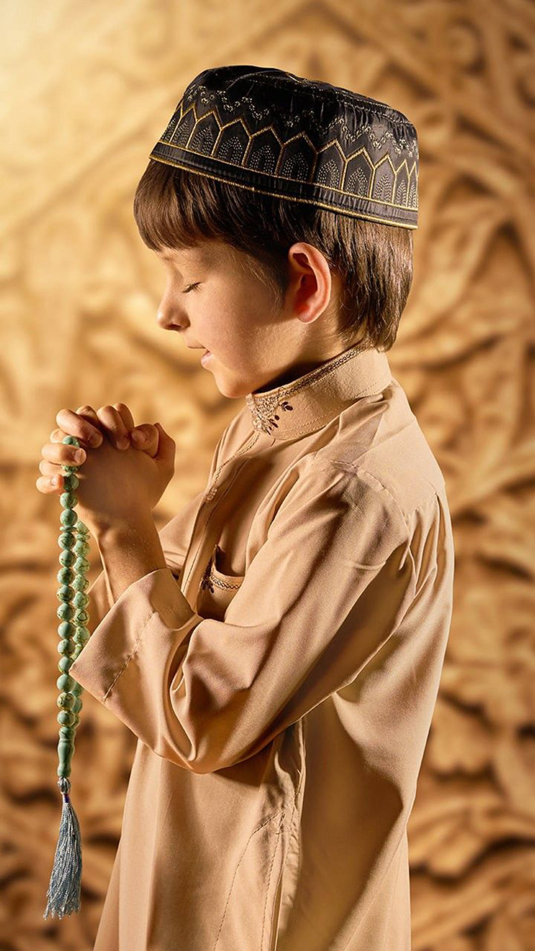 祈禱 桌布 壁紙 — 一個穿著傳統服飾的男孩，手持綠色念珠，在金色華麗的牆前祈禱。