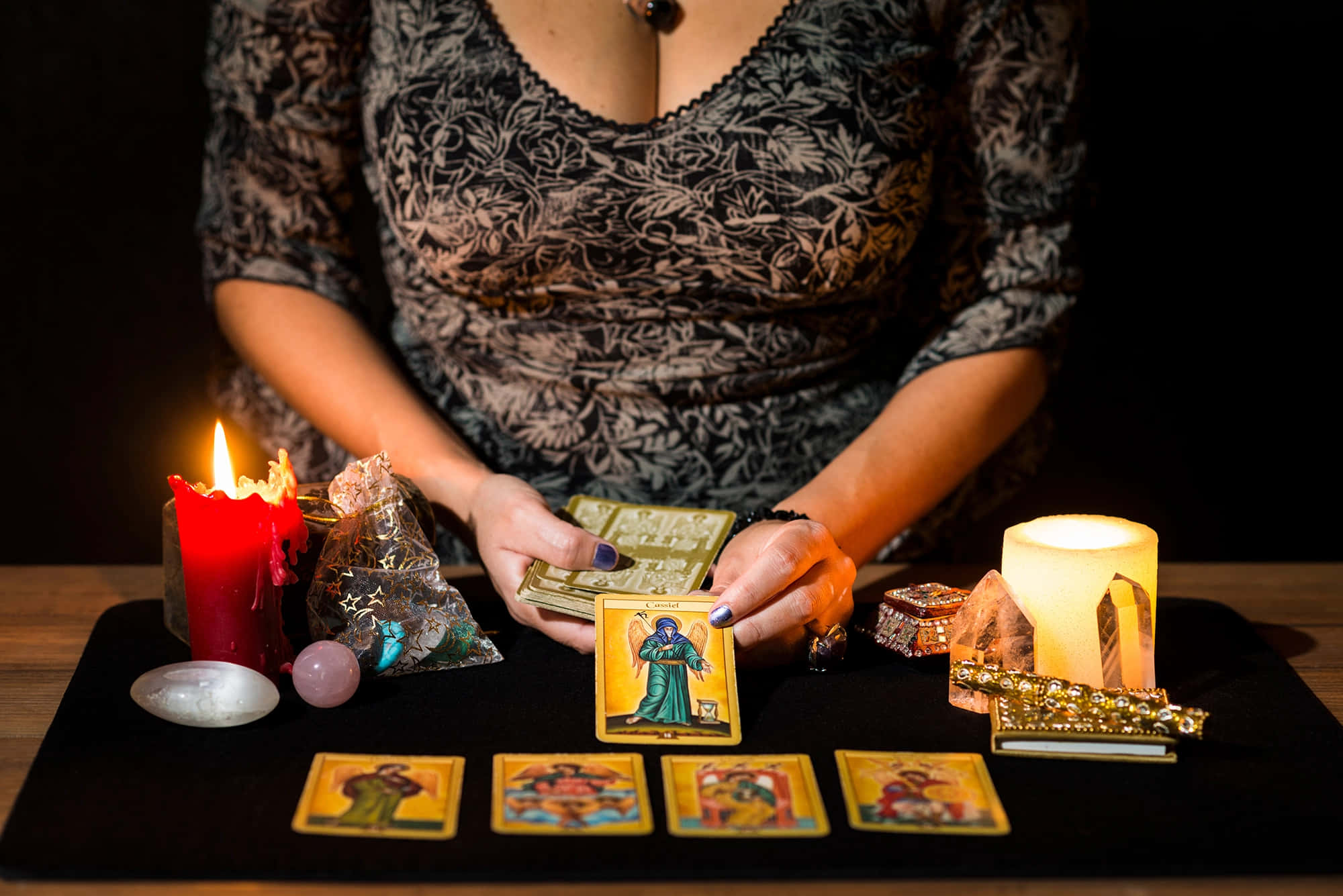 Fortune Teller 桌布 壁紙 — 一個穿著圖案上衣的人手持塔羅牌，放在由蠟燭和水晶照亮的暗色桌子上方。