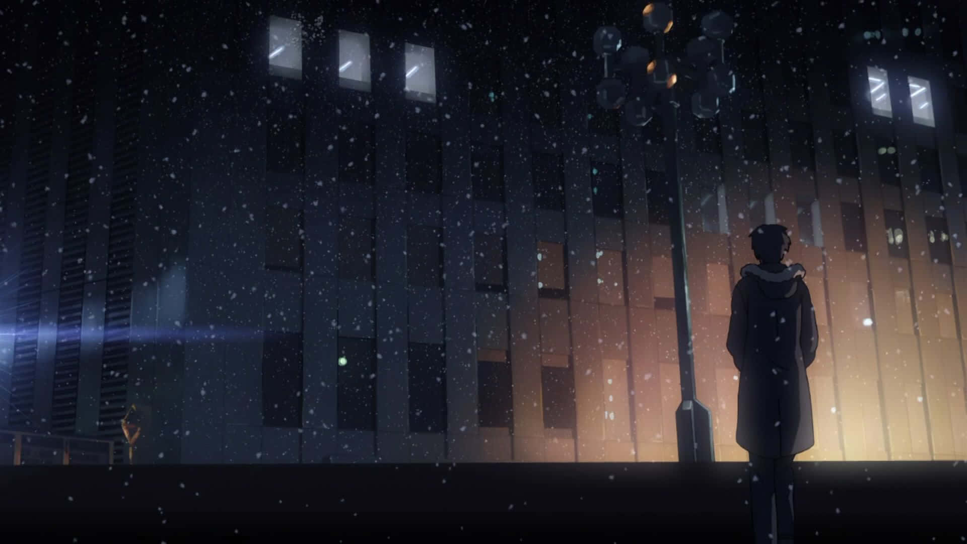 Makoto Shinkai 桌布 壁紙 — 一個穿著外套的孤獨身影站在街燈下，雪花飄落，背景是夜間發光的城市建築。