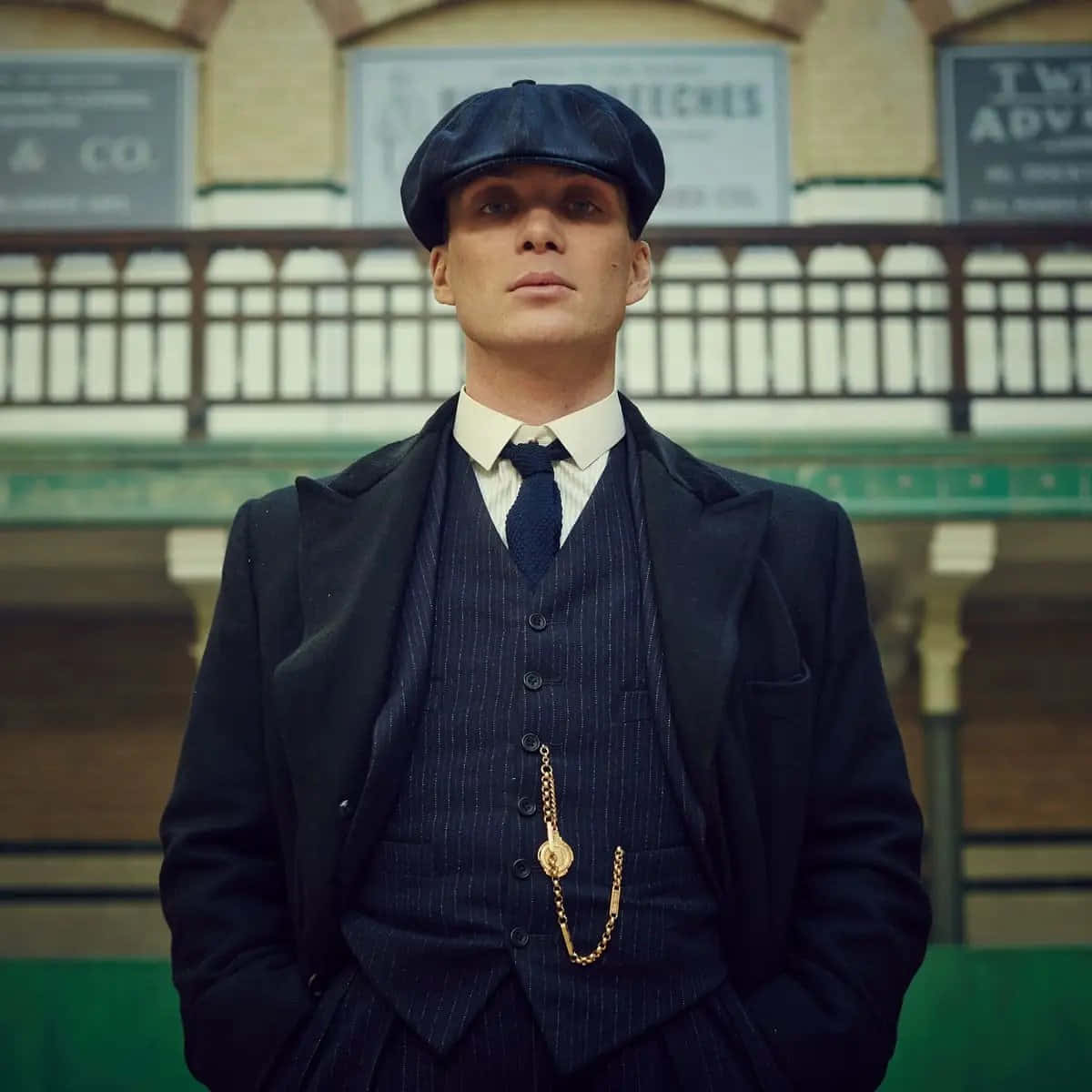 Peaky Blinders 桌布 壁紙 — 一個穿著尖條紋西裝和扁帽的男人自信地站在一個裝飾華麗的復古火車站裡。