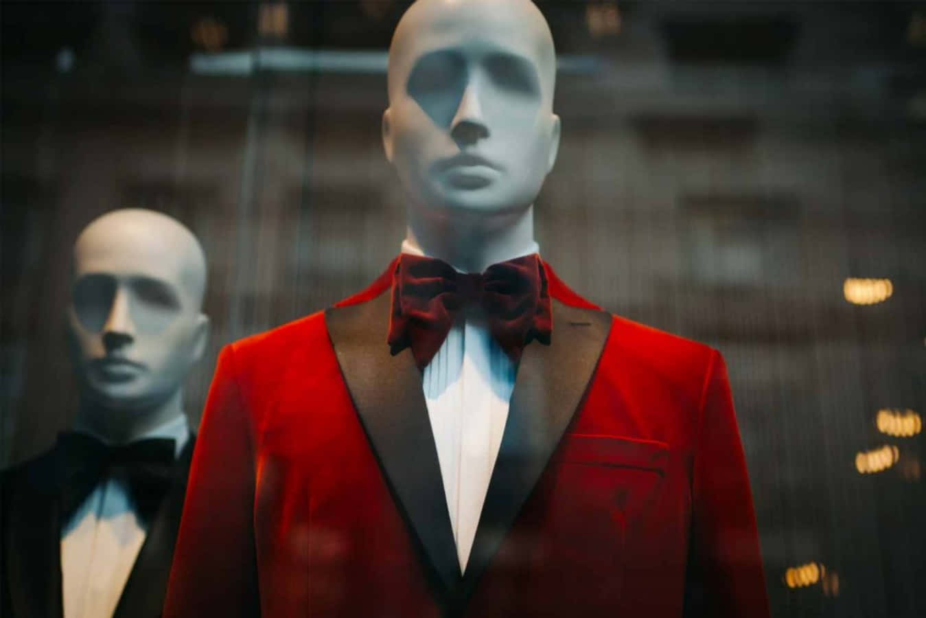 Black Tie Event 桌布 壁紙 — 一個穿著搶眼紅色天鵝絨禮服配酒紅色領結的人體模型站在商店櫥窗裡，反射著夜晚的城市燈光。