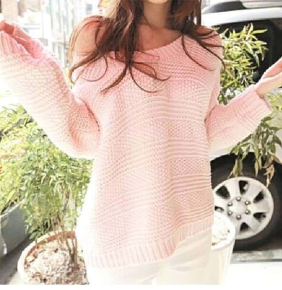 Pink Sweater 桌布 壁紙 — 一個穿著柔軟粉紅色針織毛衣的人，在戶外張開雙臂，靠近盆栽植物和一輛汽車。