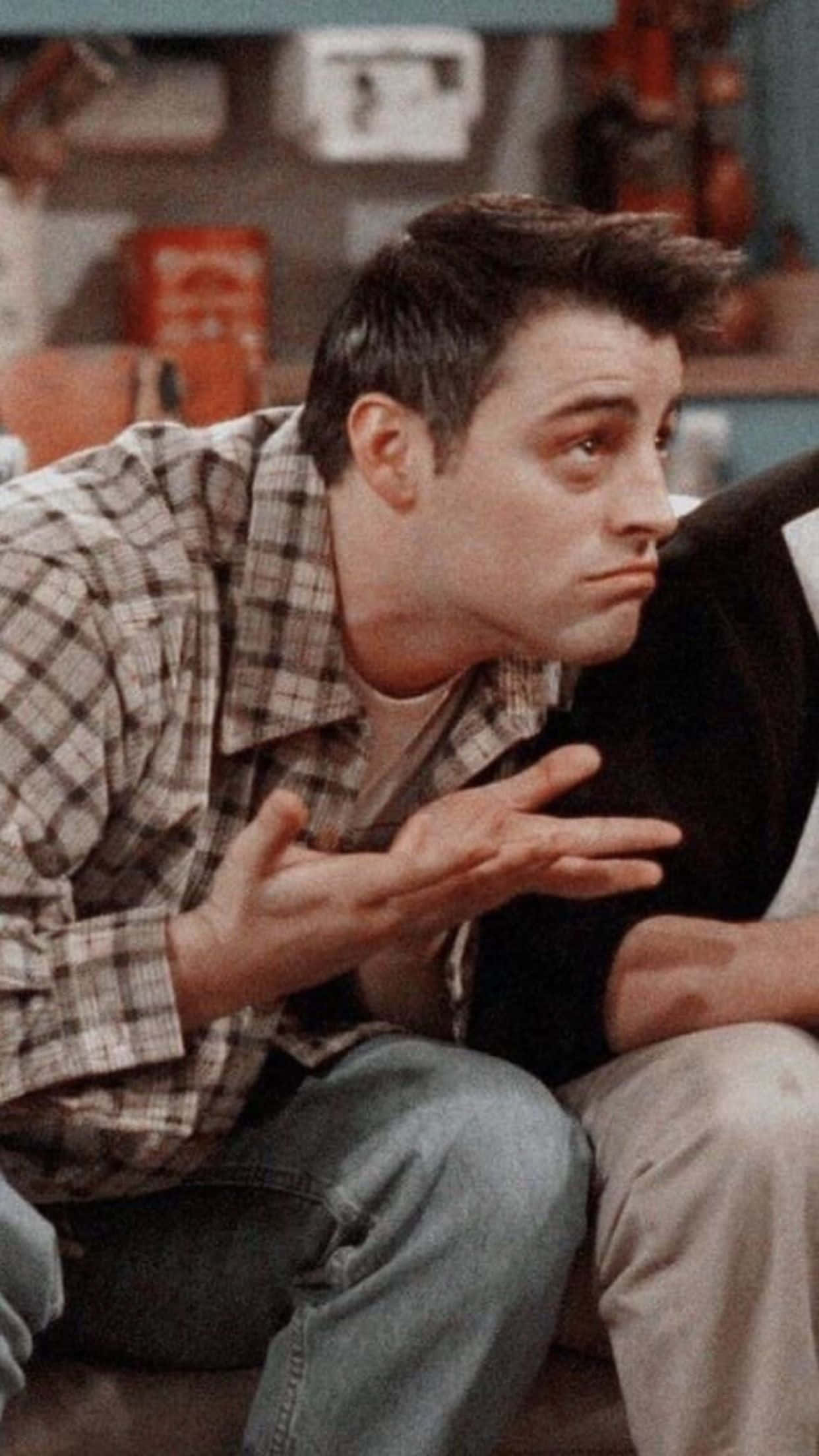 Matt Leblanc 桌布 壁紙 — 一個穿著格仔恤衫嘅男人喺雜亂嘅房間入面坐喺梳化上做出懇求嘅手勢。
