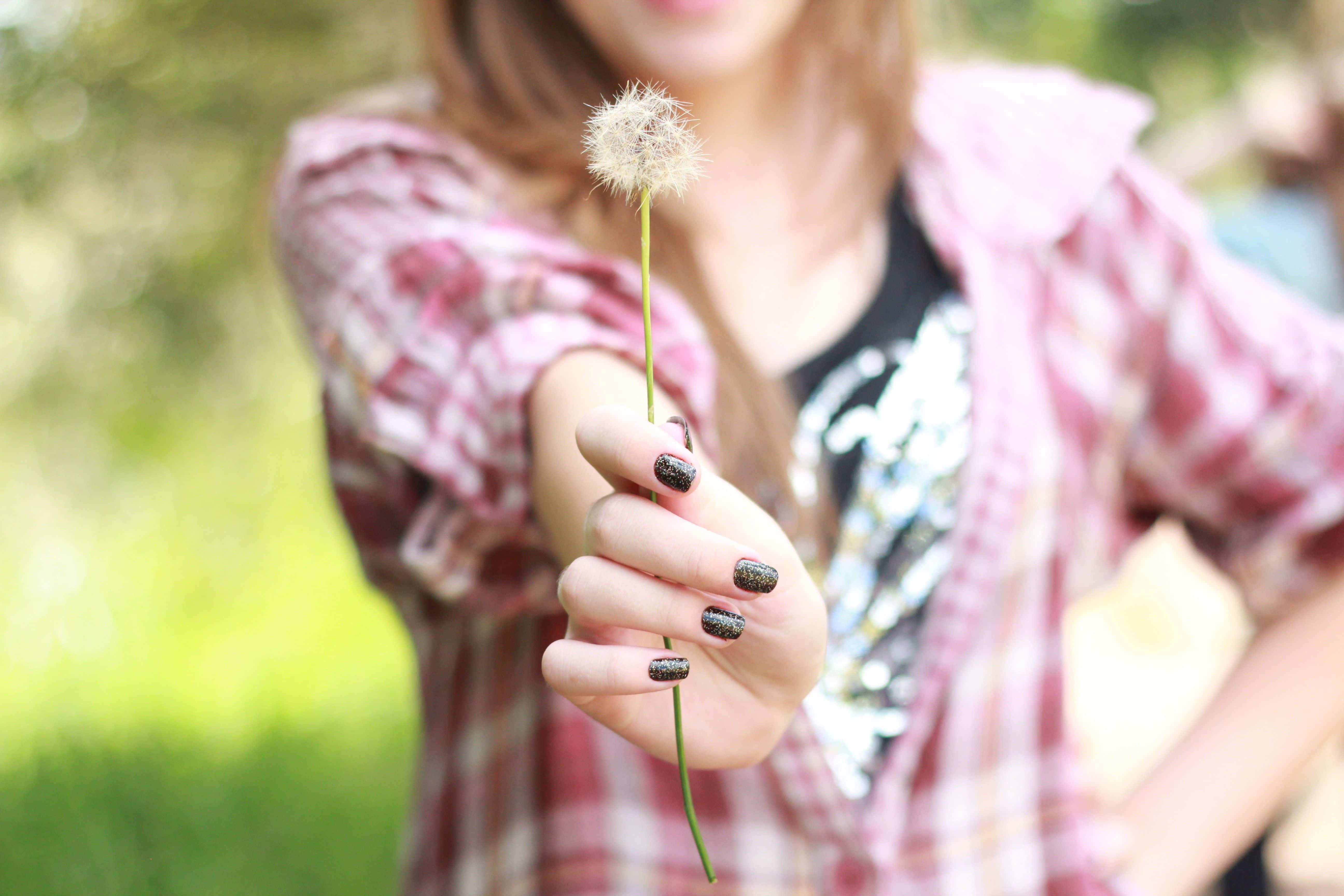 Spring Nails 桌布 壁紙 — 一個穿著格仔衫嘅人喺柔和嘅綠色模糊背景前伸出一個蒲公英種子球。