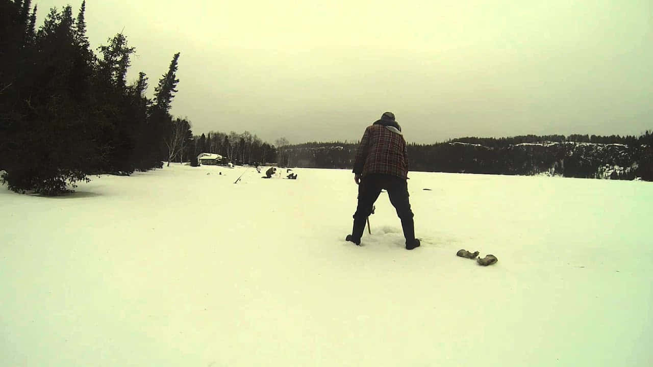 Ice Fishing 桌布 壁紙 — 一個穿著格子外套嘅孤獨人行過一個廣闊嘅雪地，有常青樹同遠處嘅山丘，天空多雲。