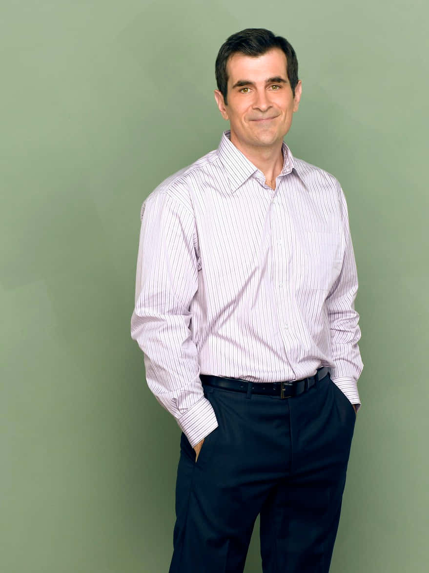 Ty Burrell 桌布 壁紙 — 一個穿著條紋襯衫和深色褲子的男人，雙手插袋，自信地站在純綠色攝影棚背景前。