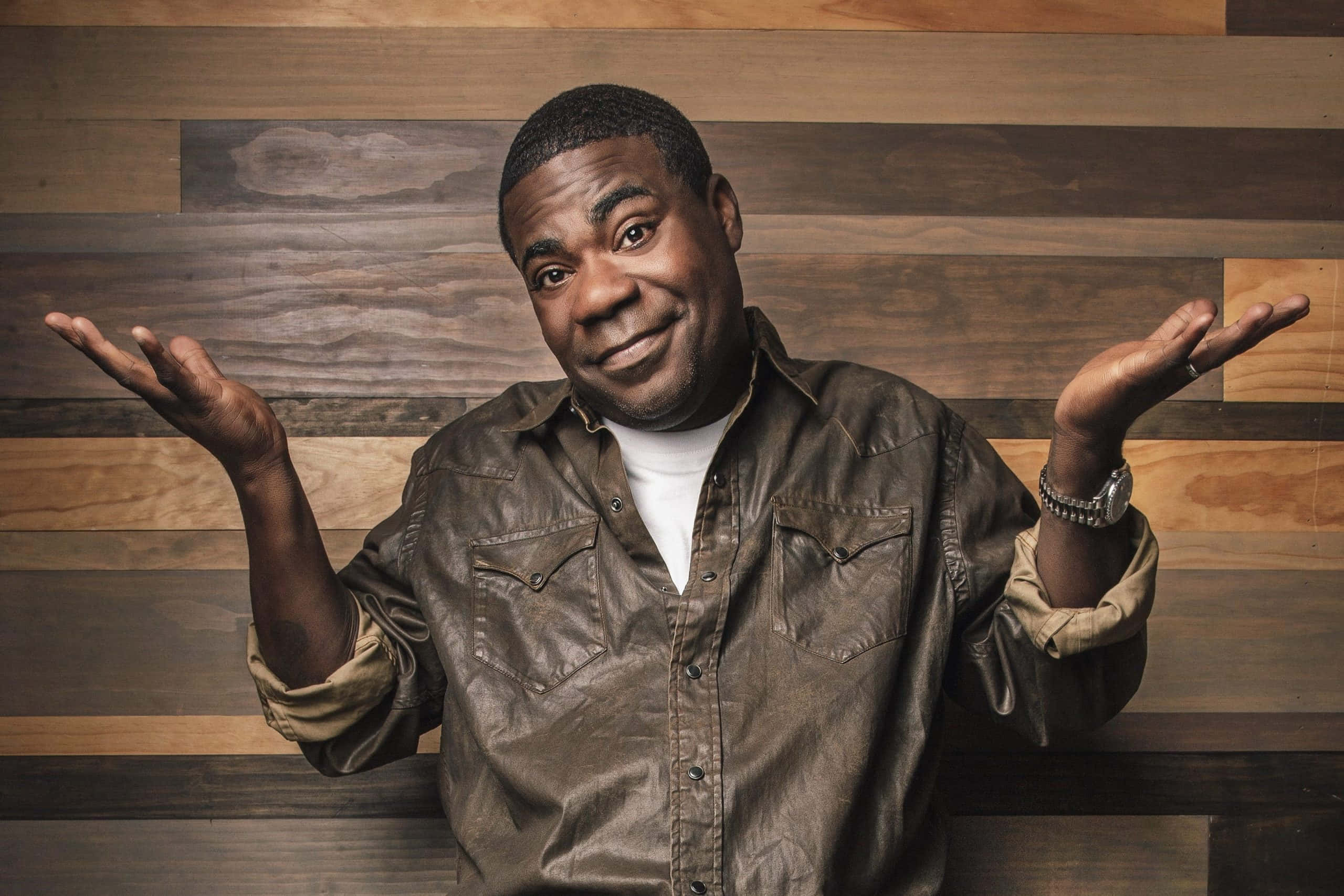 Tracy Morgan 桌布 壁紙 — 一個穿著棕色皮襯衫的男人，對著木板牆張開手掌聳肩。