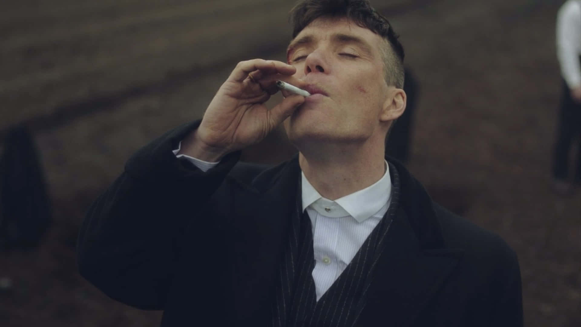 Peaky Blinders 桌布 壁紙 — 一個穿著深色外套和白色襯衫的男人，在模糊的大地色背景下閉著眼睛抽煙。