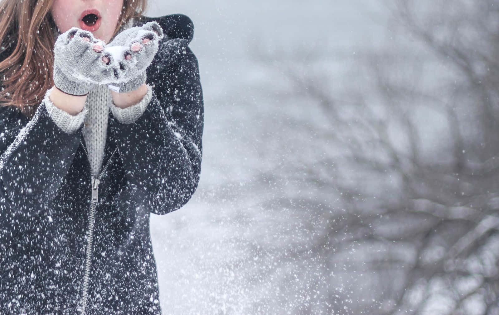 Winter Fashion 桌布 壁紙 — 一個穿著深色外套和貓咪主題手套的孩子，在雪白的冬季背景下開心地將雪拋向空中。