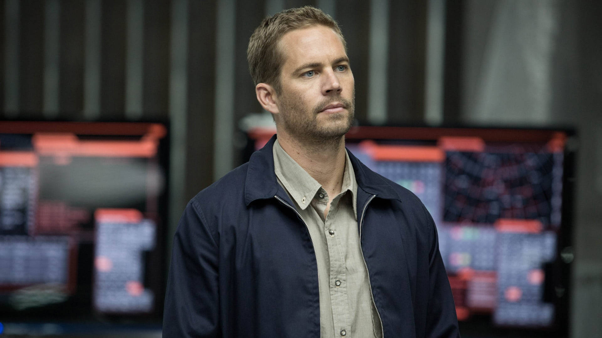 Paul Walker 桌布 壁紙 — 一個穿著深色外套的男人站在一個高科技控制室內，身後有發光的屏幕。
