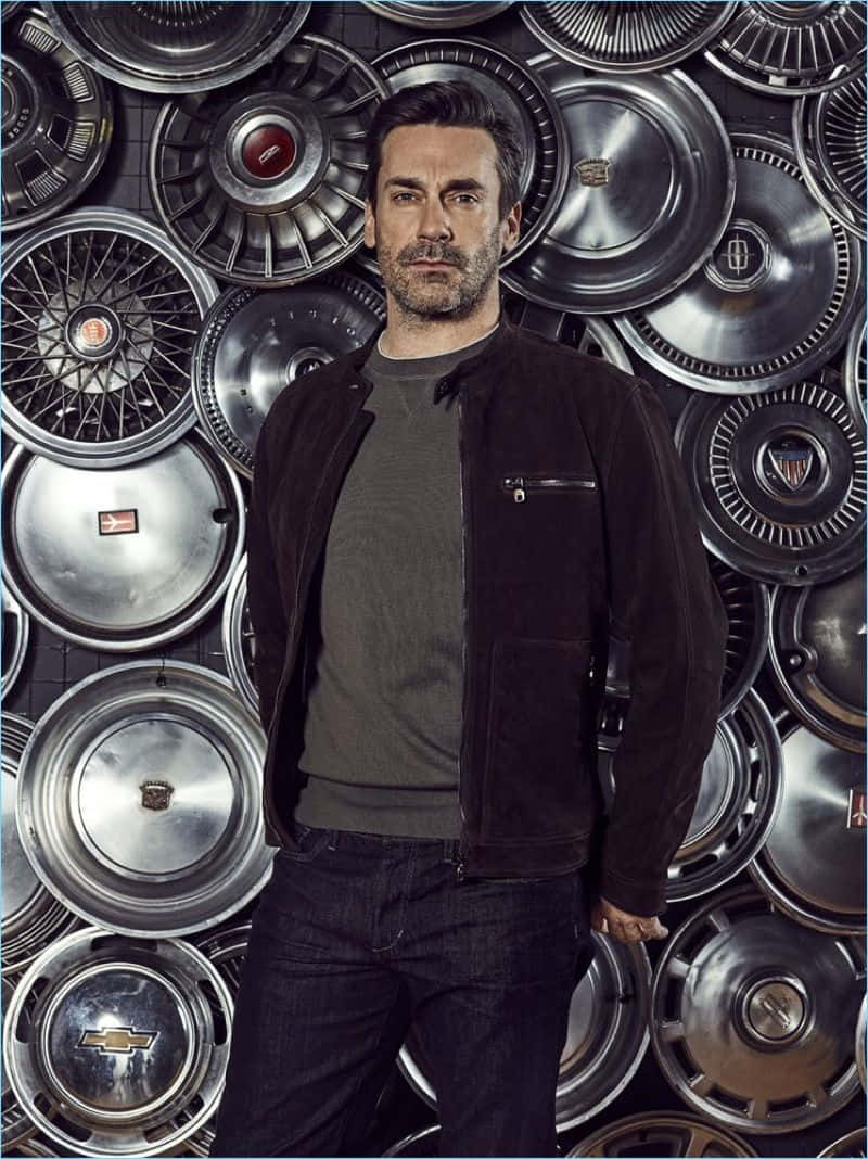 Jon Hamm 桌布 壁紙 — 一個穿著深色外套的男人自信地站在一堵復古鍍鉻汽車輪轂蓋牆前。