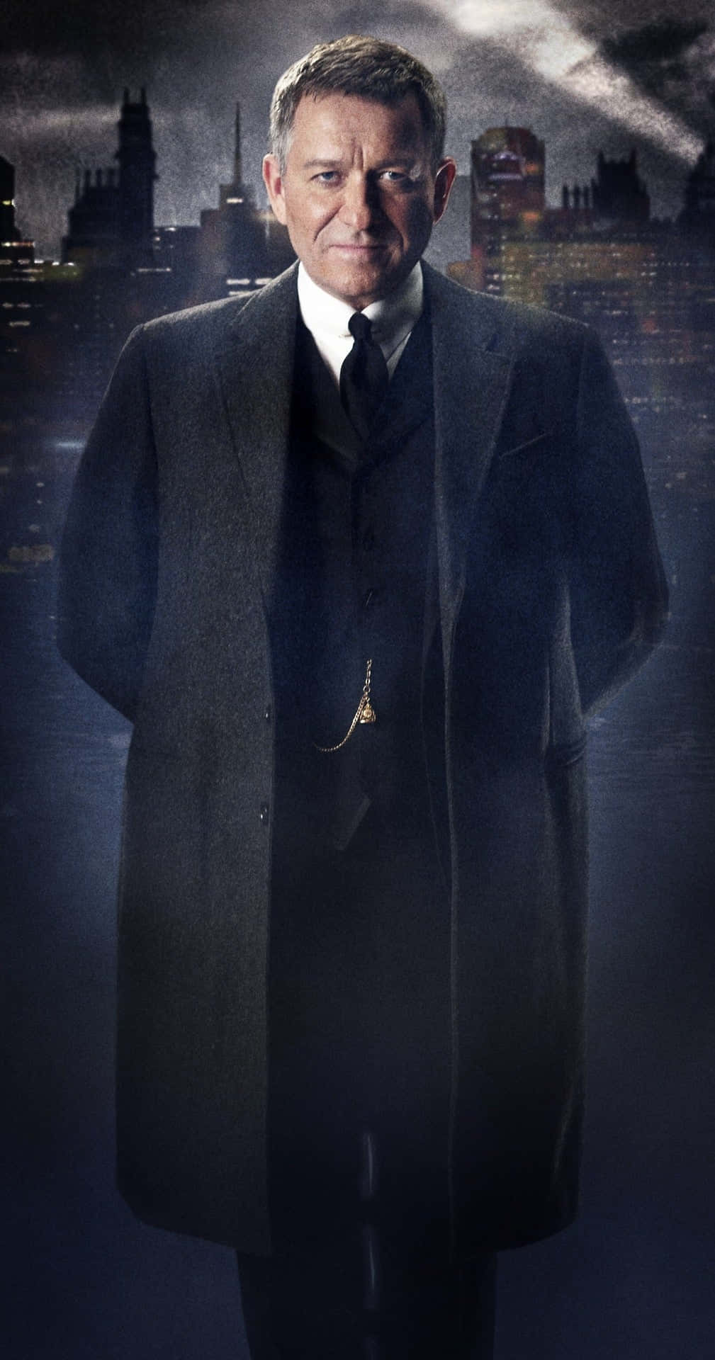 Alfred Pennyworth 桌布 壁紙 — 一個穿著深色大衣的男人在夜晚戲劇性的燈光下，莊嚴地站在陰鬱的城市天際線前。