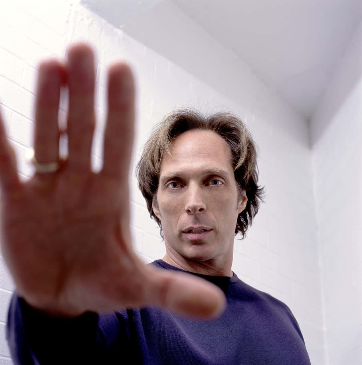 William Fichtner 桌布 壁紙 — 一個穿著深色襯衫的男人，手指上戴著戒指，對著白色磚牆伸出手。