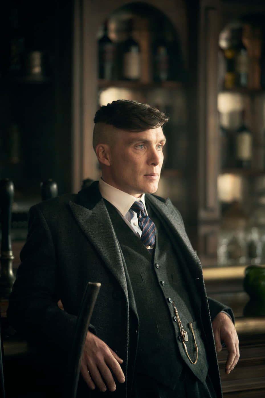 Peaky Blinders 桌布 壁紙 — 一個穿著深色西裝和領帶的男人站在燈光昏暗的酒吧裡，身後有擺滿酒瓶的架子。