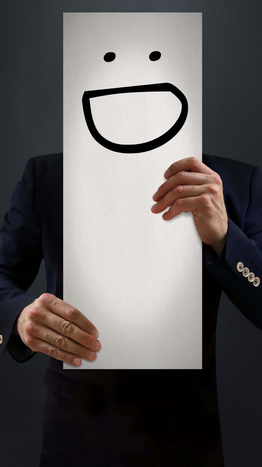 Happy iPhone 桌布 壁紙 — 一個穿著深色西裝的人，在灰色背景前舉著一塊畫有簡單黑色笑臉的白板。