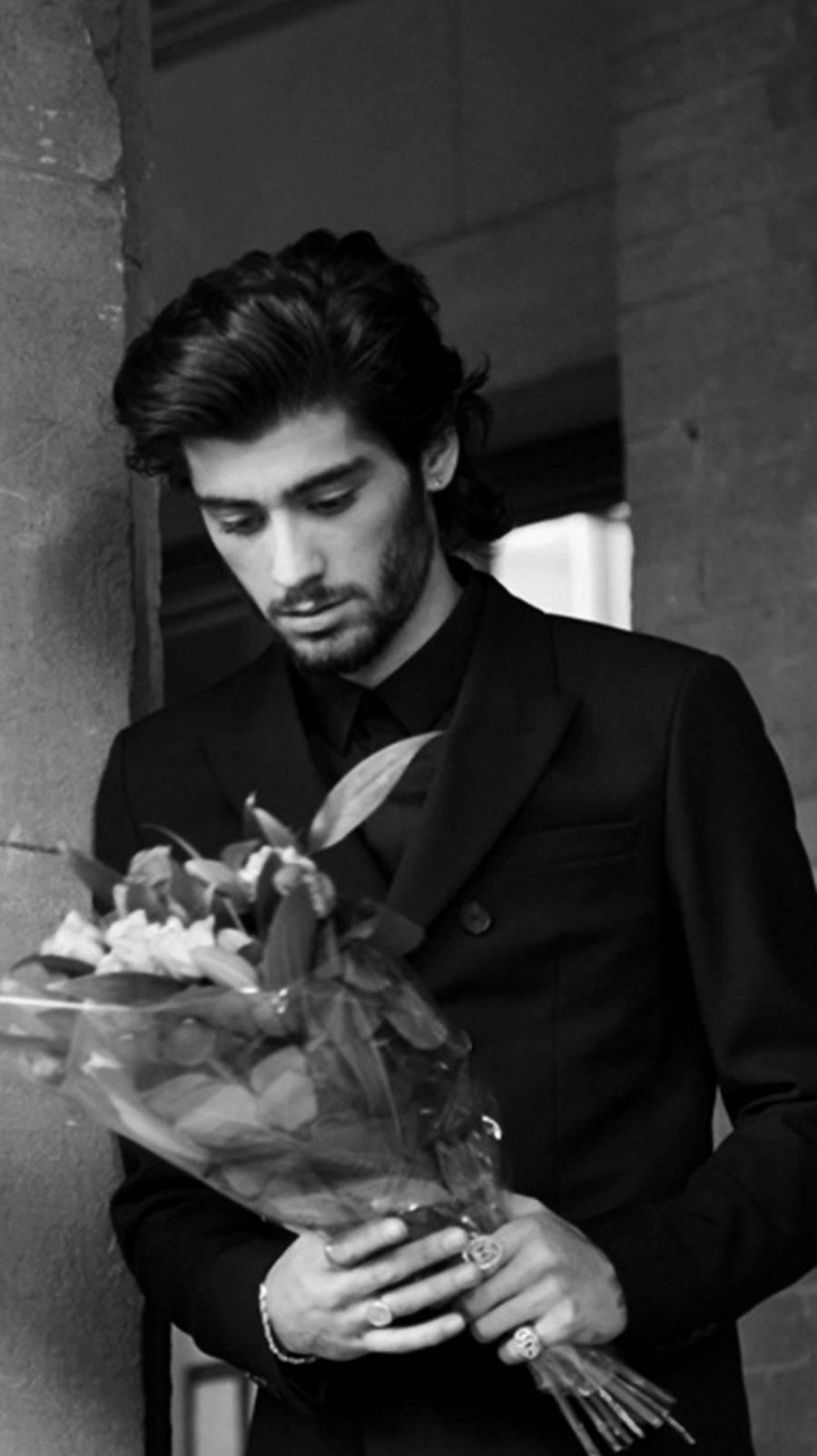 Zayn Malik 桌布 壁紙 — 一個穿著深色西裝的男人在單色城市環境中拿著一束花，低頭看著。