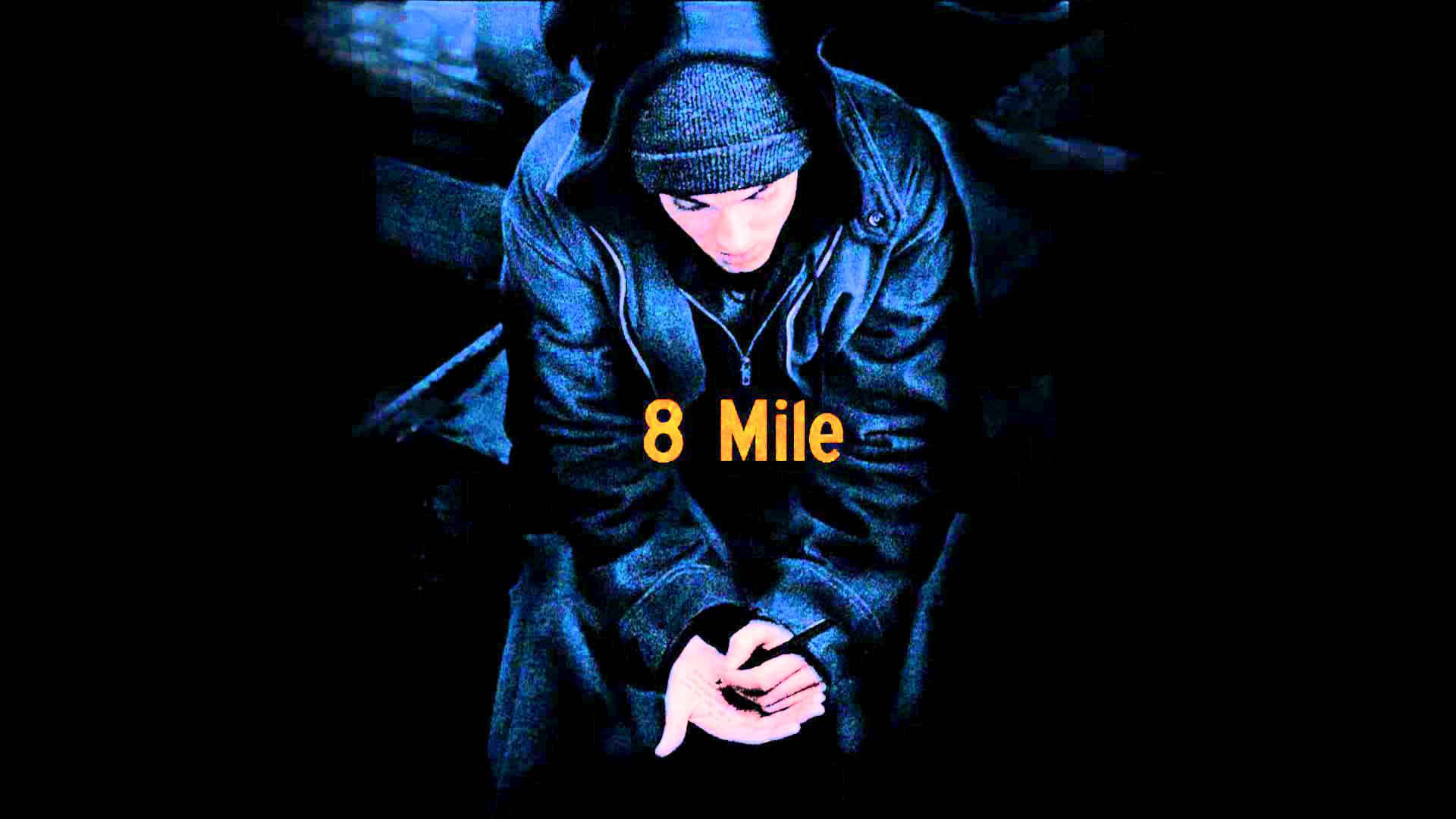 Eminem 桌布 壁紙 — 一個穿著深色連帽衫和冷帽的年輕男子，在陰影藍光中彎腰坐著，手持一支筆，'8 Mile' 文字發出黃色光芒。