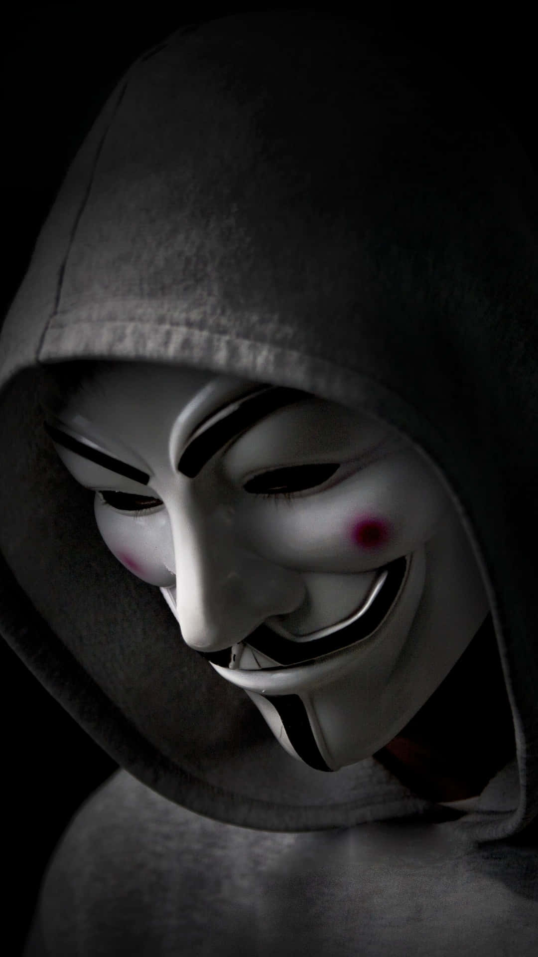 Anonymous 桌布 壁紙 — 一個穿著深色連帽衫的人，在黑色背景前戴著白色蓋伊·福克斯面具，臉頰上有紅色標記。