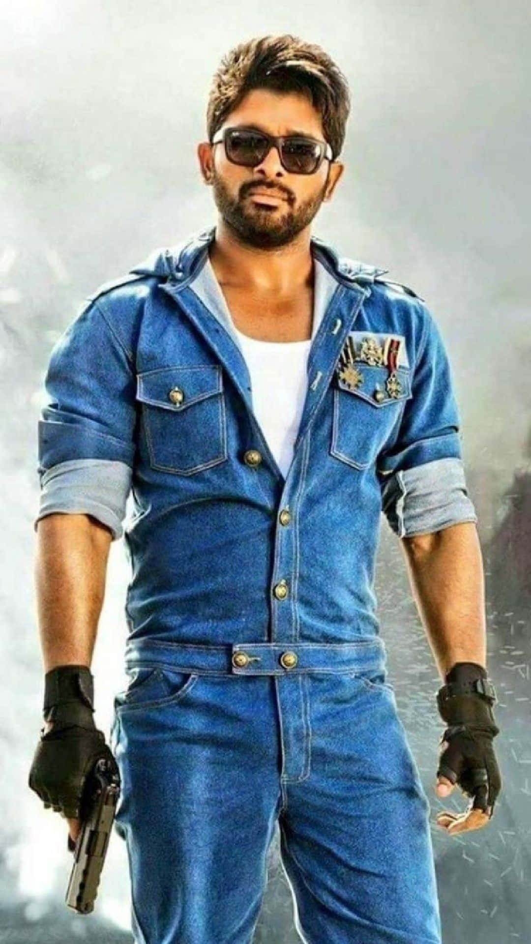 Allu Arjun 桌布 壁紙 — 一個穿著牛仔工裝褲和太陽眼鏡的男人，在煙霧灰色背景前拿著手槍。