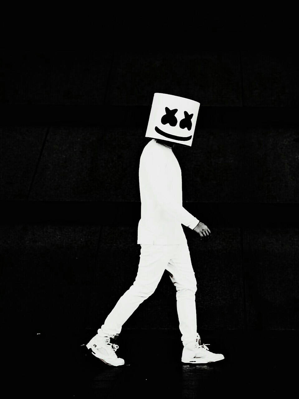marshmello iPhone 桌布 壁紙 — 一個穿著白色服裝和標誌性方形面具的人走在黑色背景前。