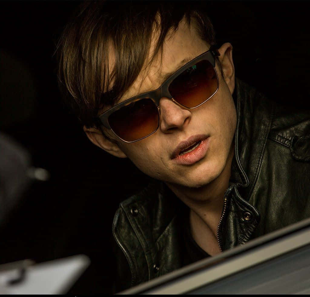 Harry Osborn 桌布 壁紙 — 一個穿著皮褸和深色太陽眼鏡的年輕男子，在昏暗的車廂內向前傾，表情嚴肅。
