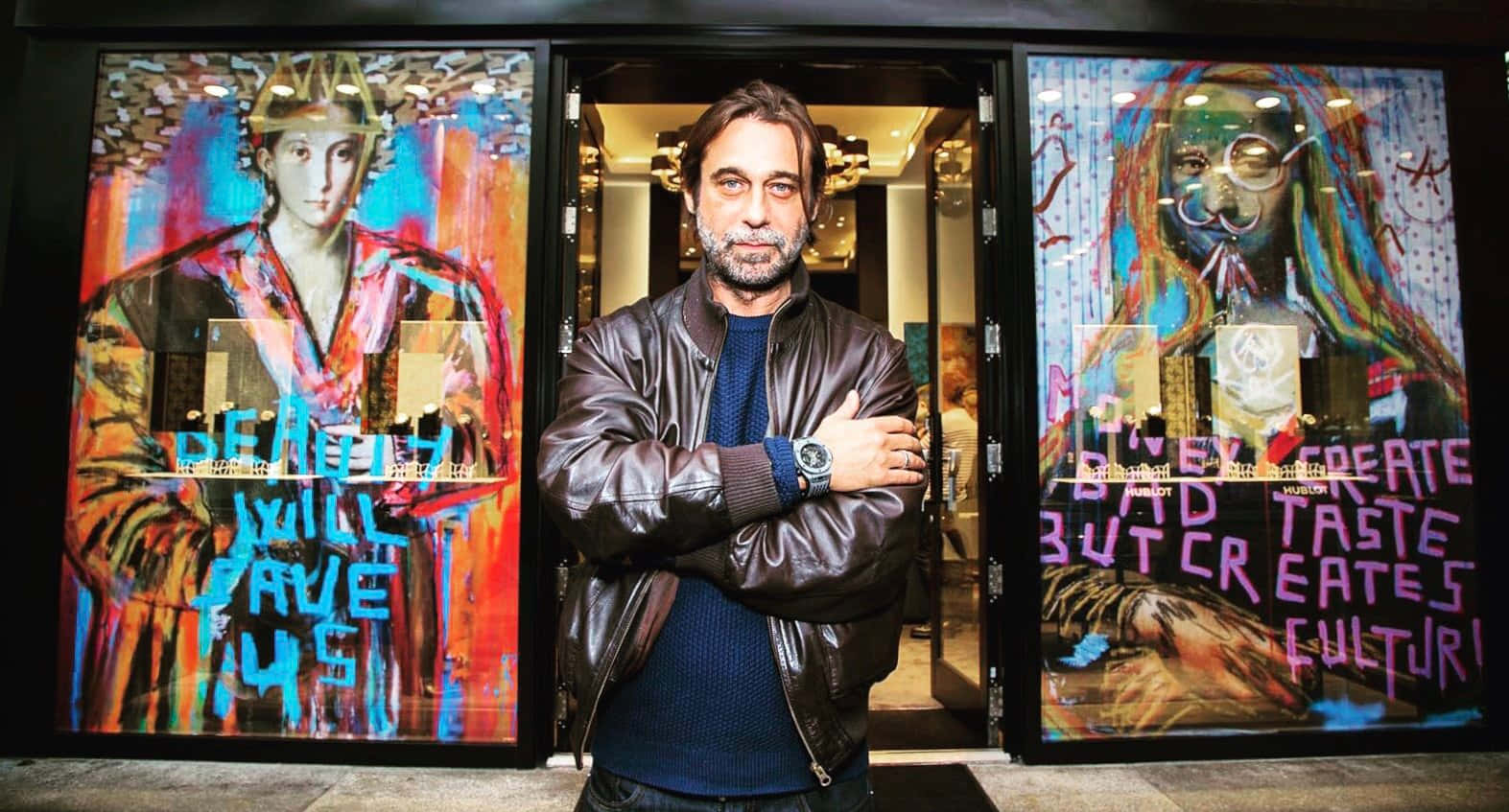 Jordi Mollà 桌布 壁紙 — 一個穿著皮褸的男人自信地交叉雙臂，站在充滿活力的塗鴉玻璃門前。