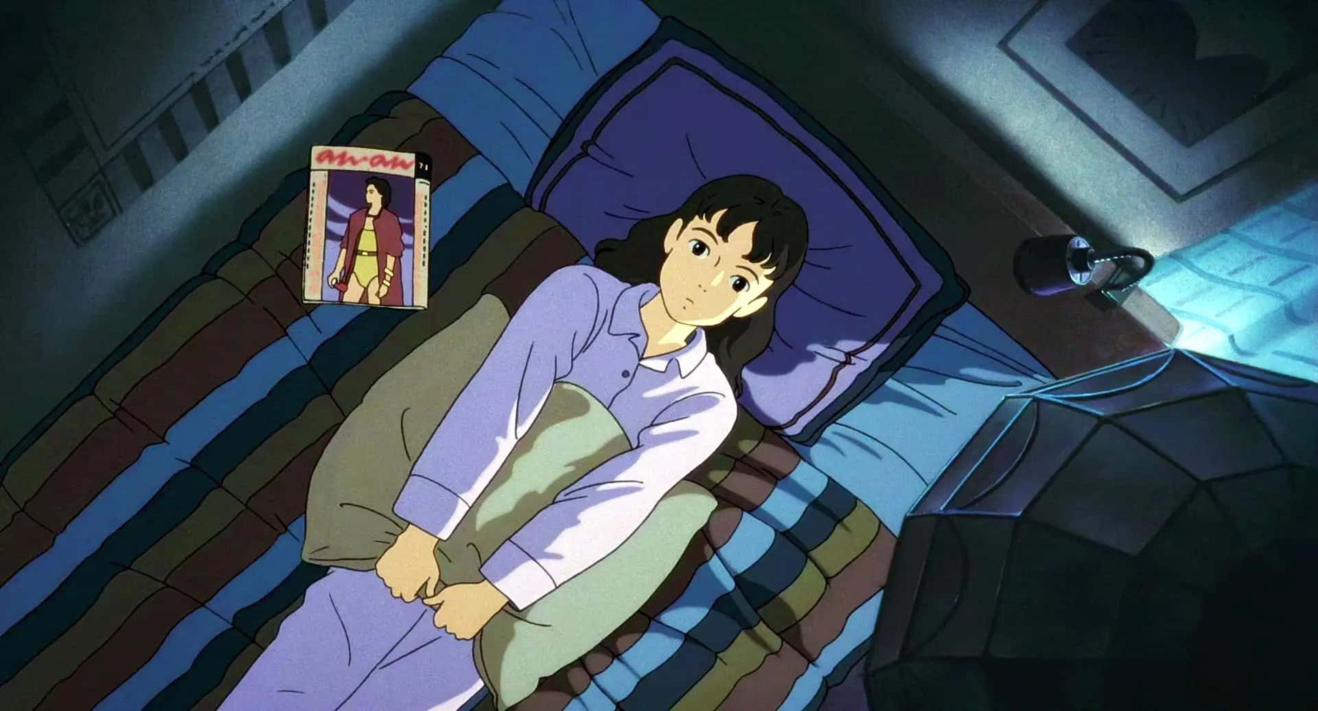 Only Yesterday 桌布 壁紙 — 一個穿著睡衣的年輕動漫女孩醒著躺在床上，蓋著條紋毯子，盯著床頭燈下發光的漫畫書。