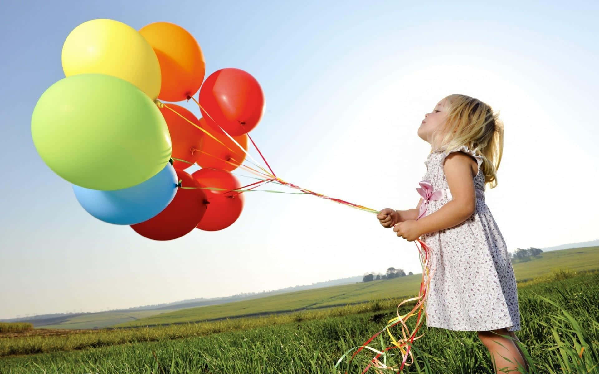 Balloon 桌布 壁紙 — 一個穿著碎花裙的小女孩在陽光明媚的日子裡，站在陽光照耀的田野上，手持一束彩色氣球。