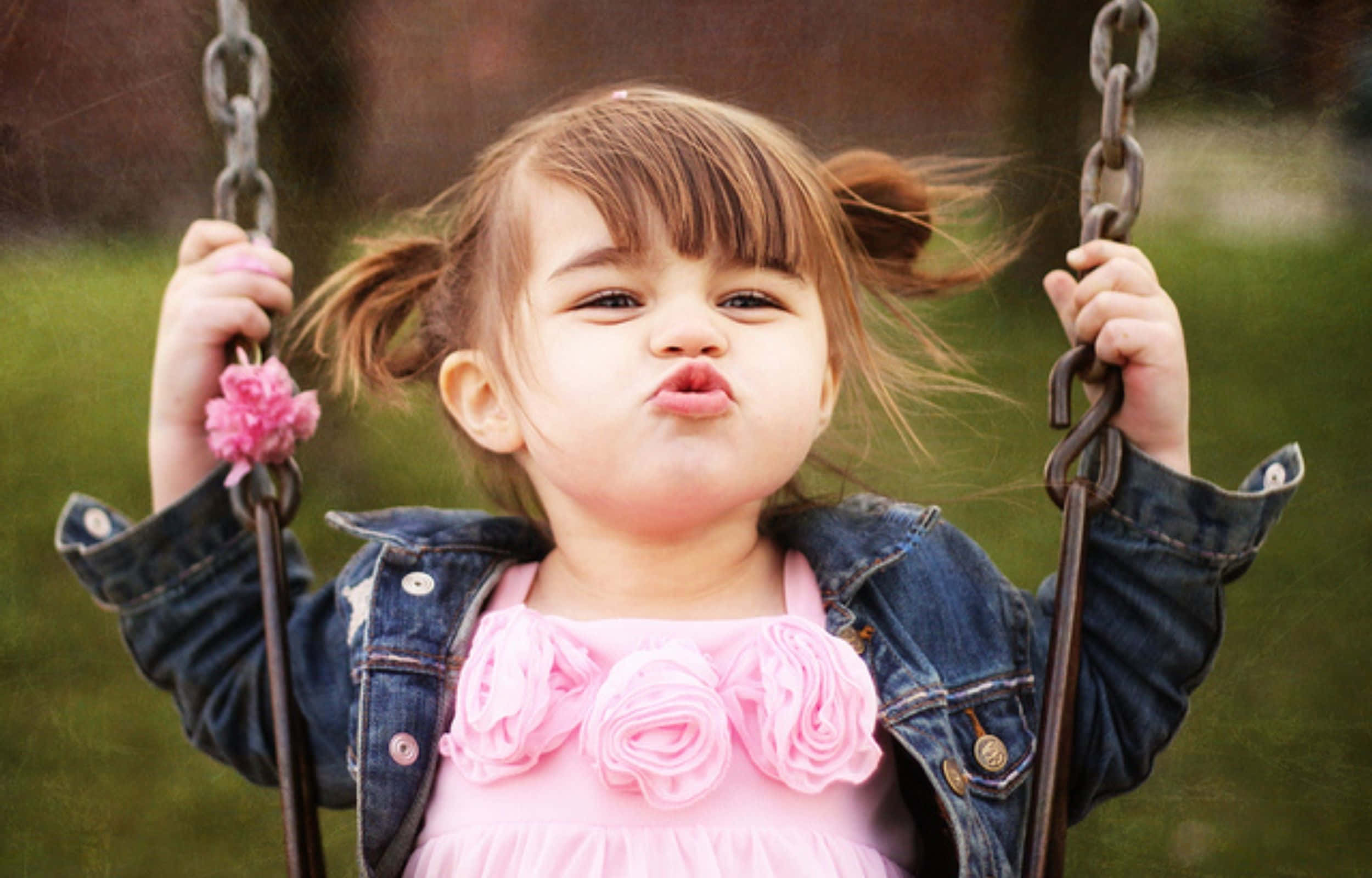 Baby Girl 桌布 壁紙 — 一個穿著粉紅色連衣裙和牛仔外套的開心幼兒，在戶外抓住鞦韆時飛吻。