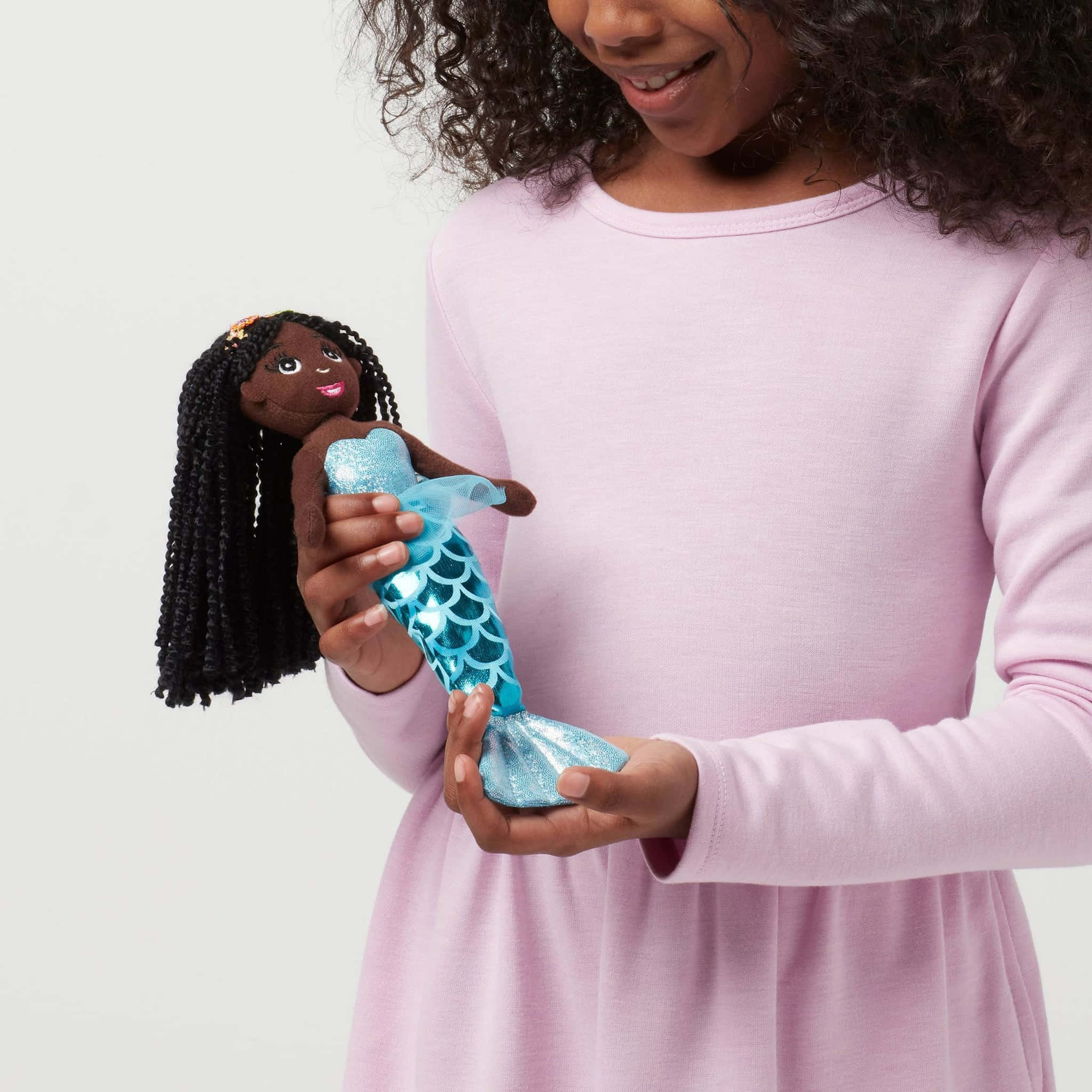 Dolls 桌布 壁紙 — 一個穿著粉紅色連衣裙的小女孩微笑著抱著一個有閃亮藍色尾巴和黑色辮子頭髮的美人魚娃娃。