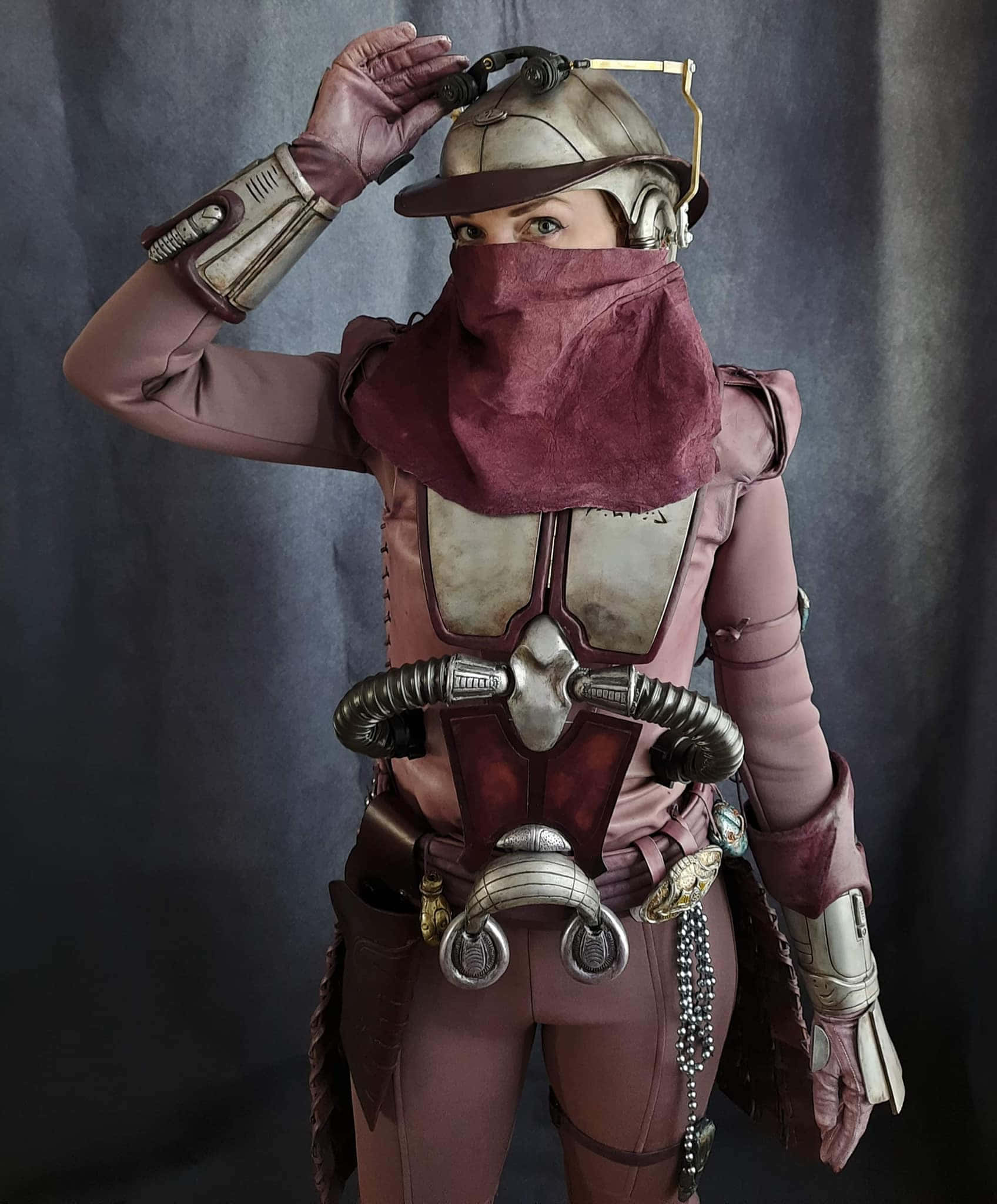 Zam Wesell 桌布 壁紙 — 一個穿著精細科幻裝甲、戴著栗色圍巾和頭盔的人，在黑暗背景下調整裝備。