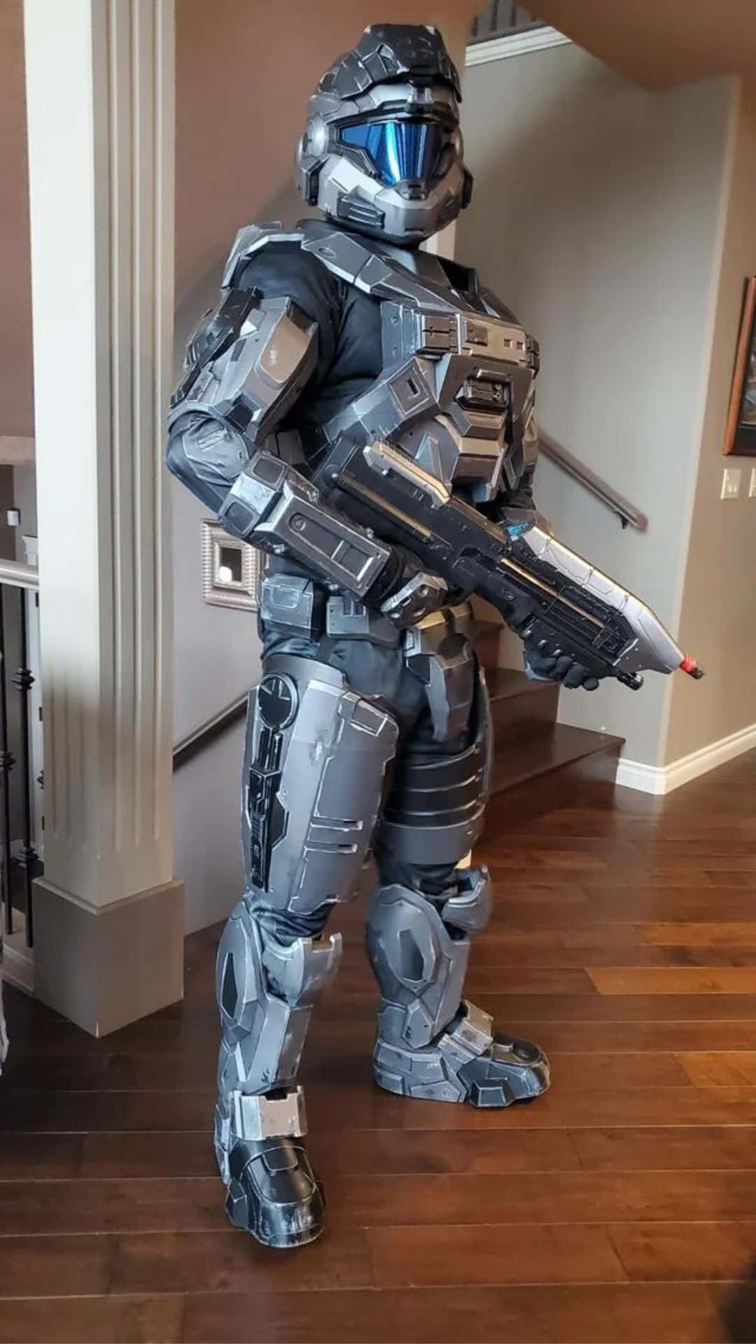 Noble Six 桌布 壁紙 — 一個穿著精細銀黑色Halo Master Chief盔甲服裝的人，在室內手持一把相配的能量步槍。