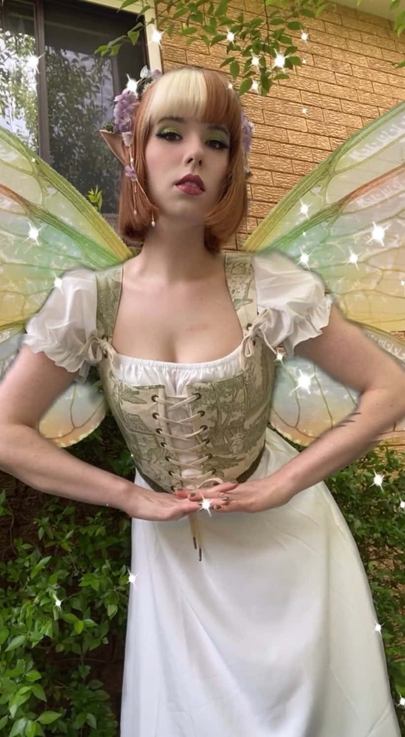 仙子美學動態圖 桌布 壁紙 — 一個穿著精緻仙女服裝、擁有半透明翅膀和花卉頭飾的人自信地站在戶外。