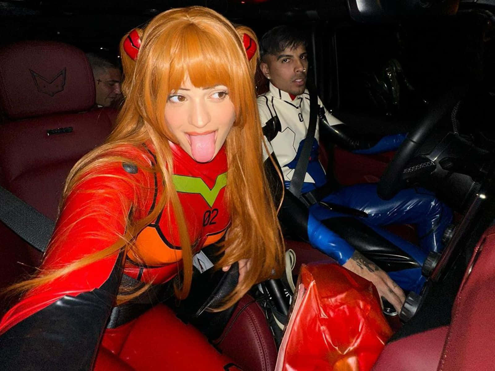 Otaku 桌布 壁紙 — 一個穿著紅色 Evangelion Unit 02 角色扮演的人伸出舌頭，與另一個穿著白色和藍色套裝的角色扮演者一起坐在紅色皮革車內。