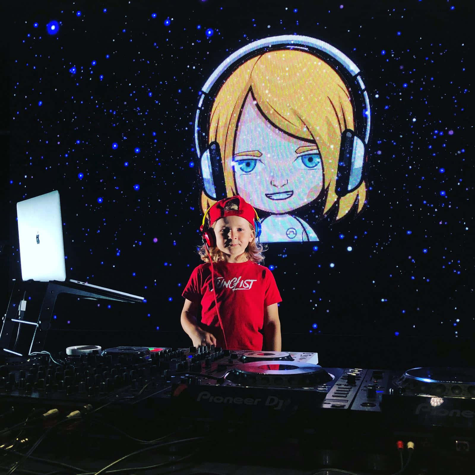 DJ 桌布 壁紙 — 一個穿著紅色襯衫和帽子的孩子站在DJ設備後面，背景是星空，有一個大型動漫女孩投影。