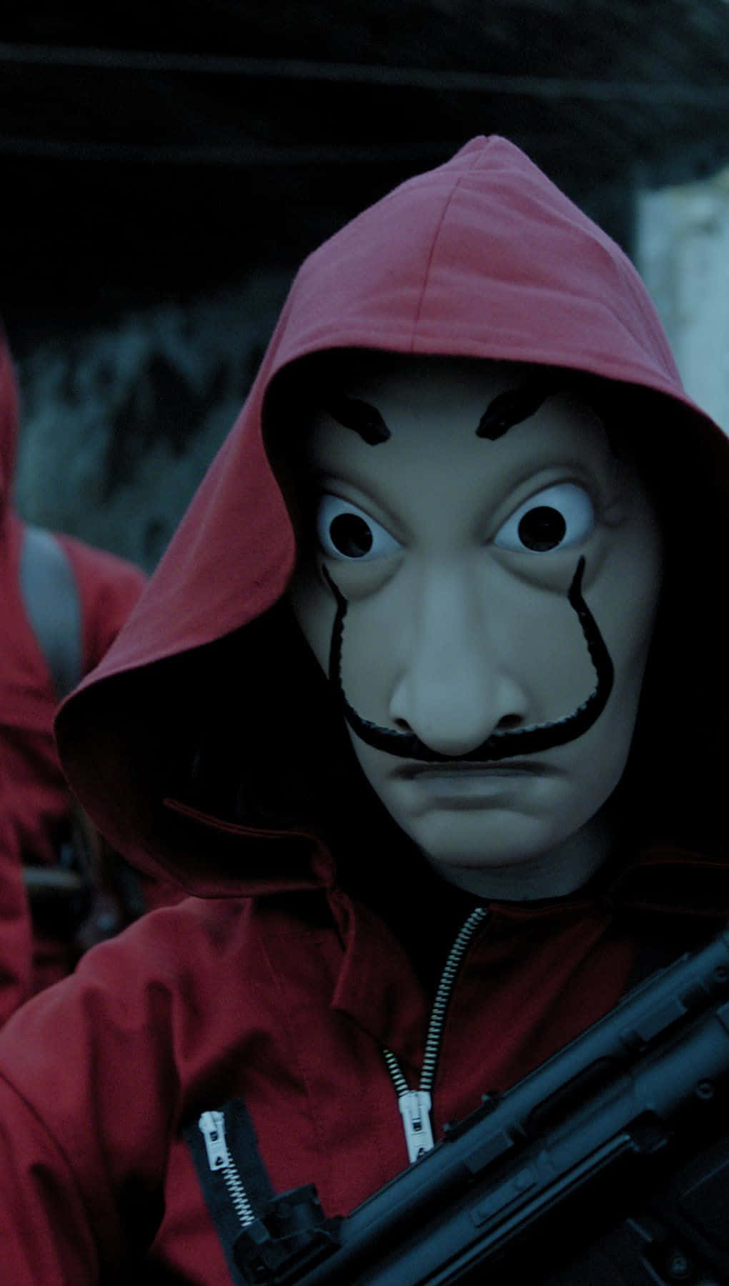 Money Heist 桌布 壁紙 — 一個穿著紅色連帽外套的人戴著白色面具，面具上有黑色鬍子，在昏暗的環境中拿著步槍。