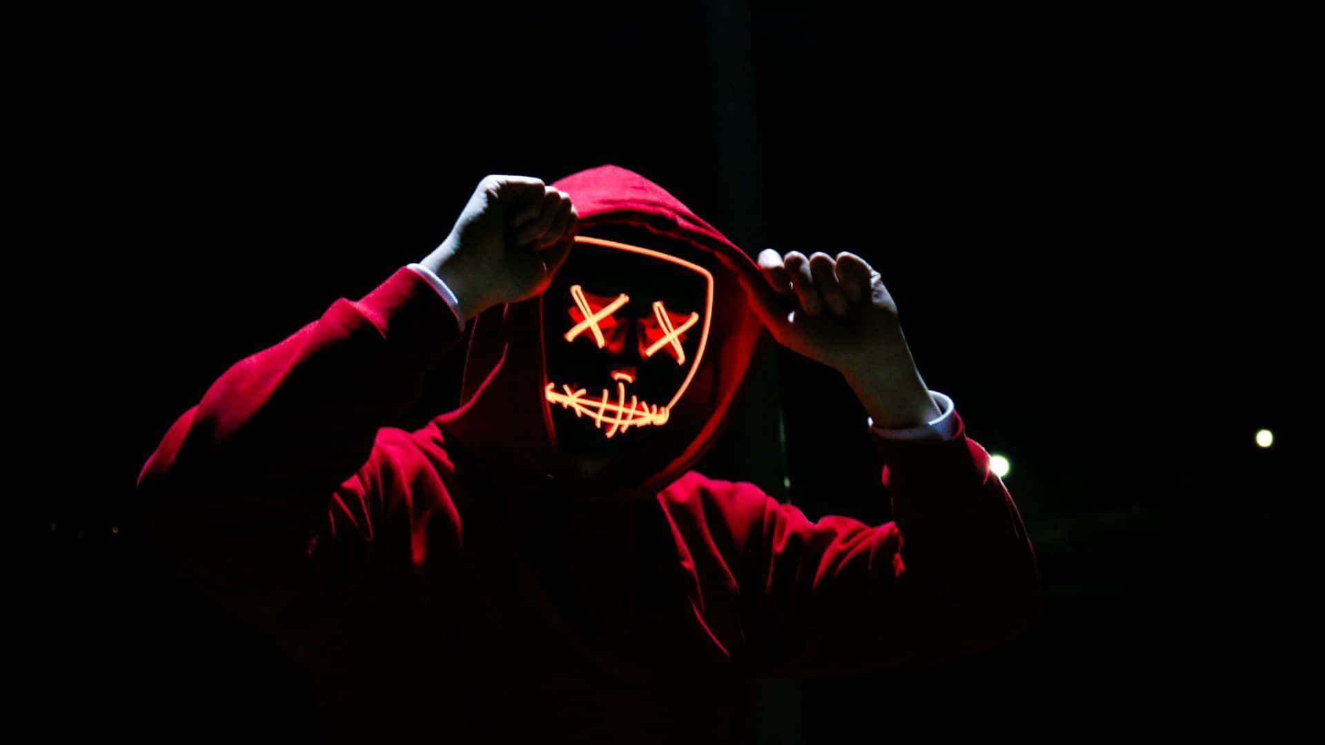 Red Hoodie 桌布 壁紙 — 一個穿著紅色連帽衫的人拉下帽子，露出一個發光的橙色LED面具，帶有X形眼睛和縫合的嘴巴，背景為黑暗。