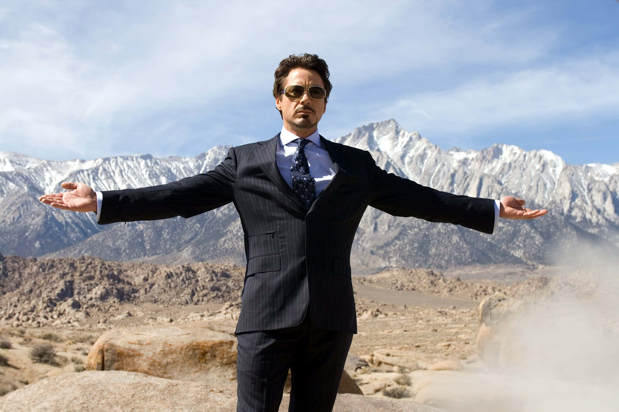 Superhero Movies 桌布 壁紙 — 一個穿著細條紋西裝和太陽眼鏡的男人在沙漠峽谷中張開雙臂站立，身後是積雪覆蓋的山脈。