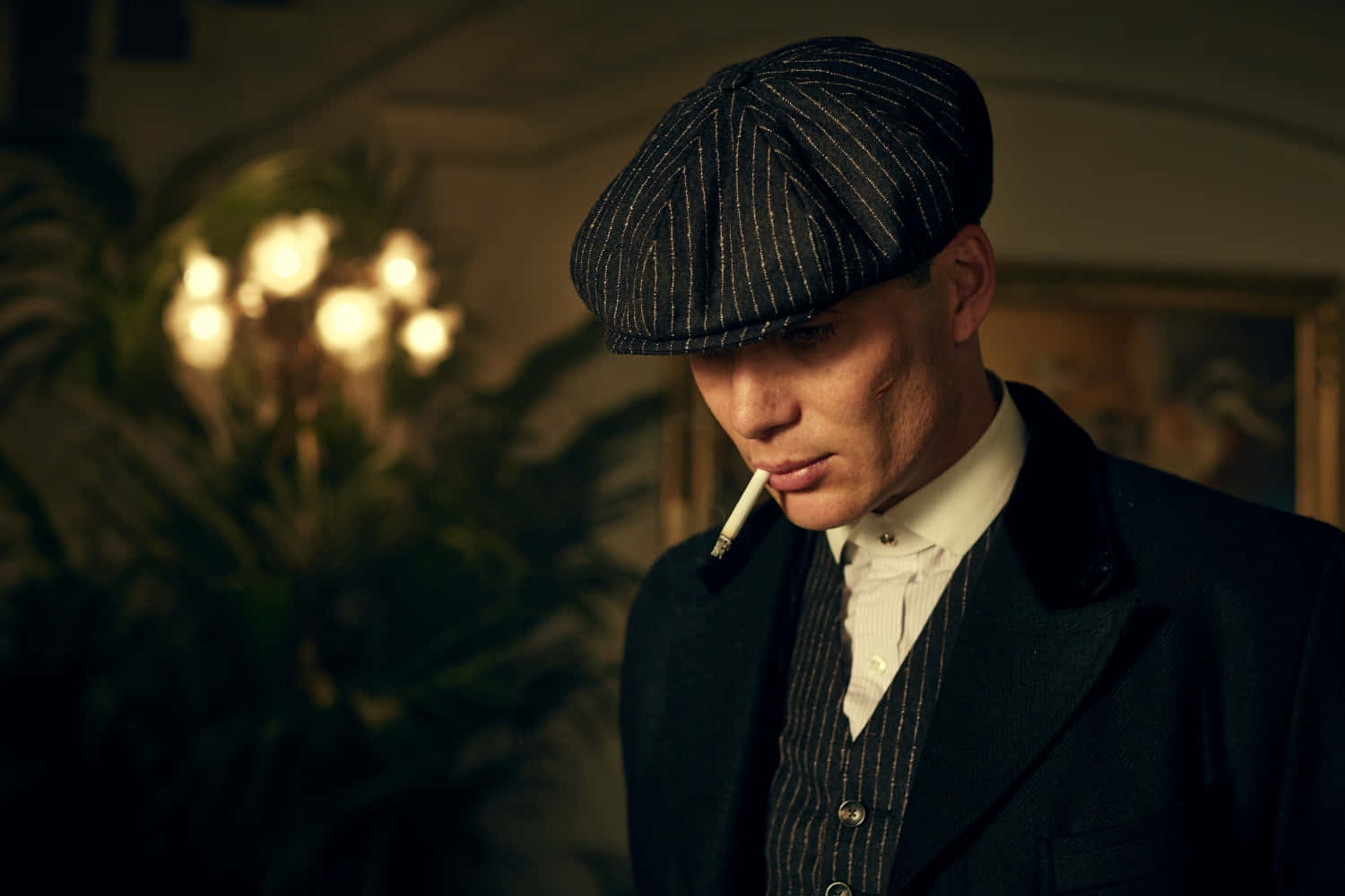 Peaky Blinders 桌布 壁紙 — 一個穿著細條紋西裝和扁帽的男人在昏暗的房間裡抽煙，身後有溫暖發光的燈光。